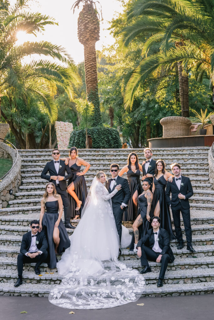 Portrait of the wedding party on the stone amphitheatre steps, bridesmaids in black gowns and groomsmen in black tuxedos