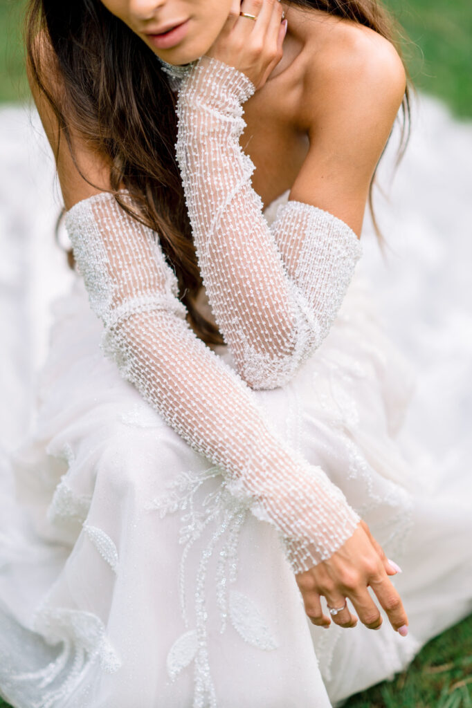 Detail of the bride's arm in a pearl-beaded lace sleeve, her engagement ring in view