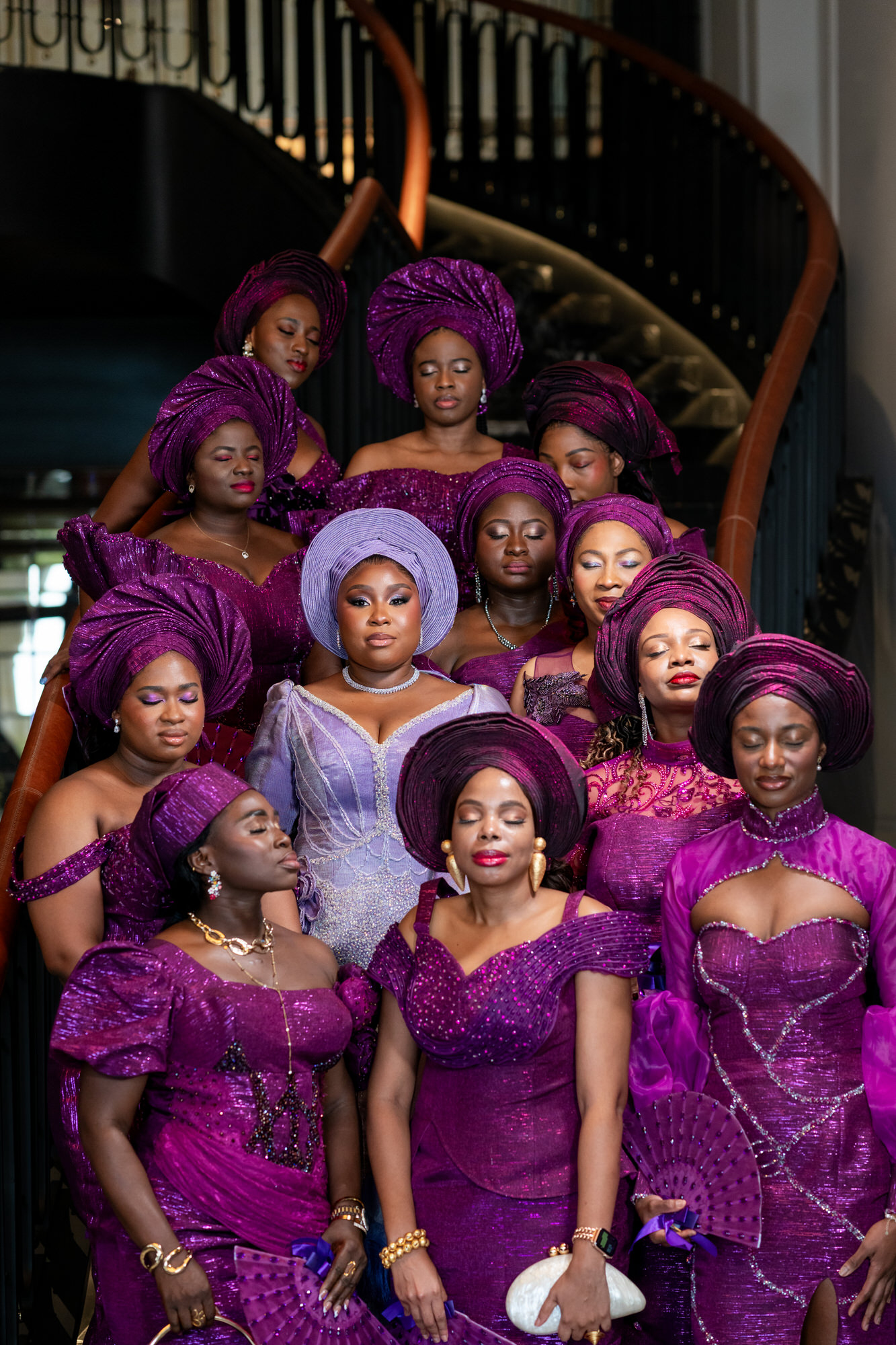 Group of women in matching purple traditional outfits and head wraps posing on a staircase.