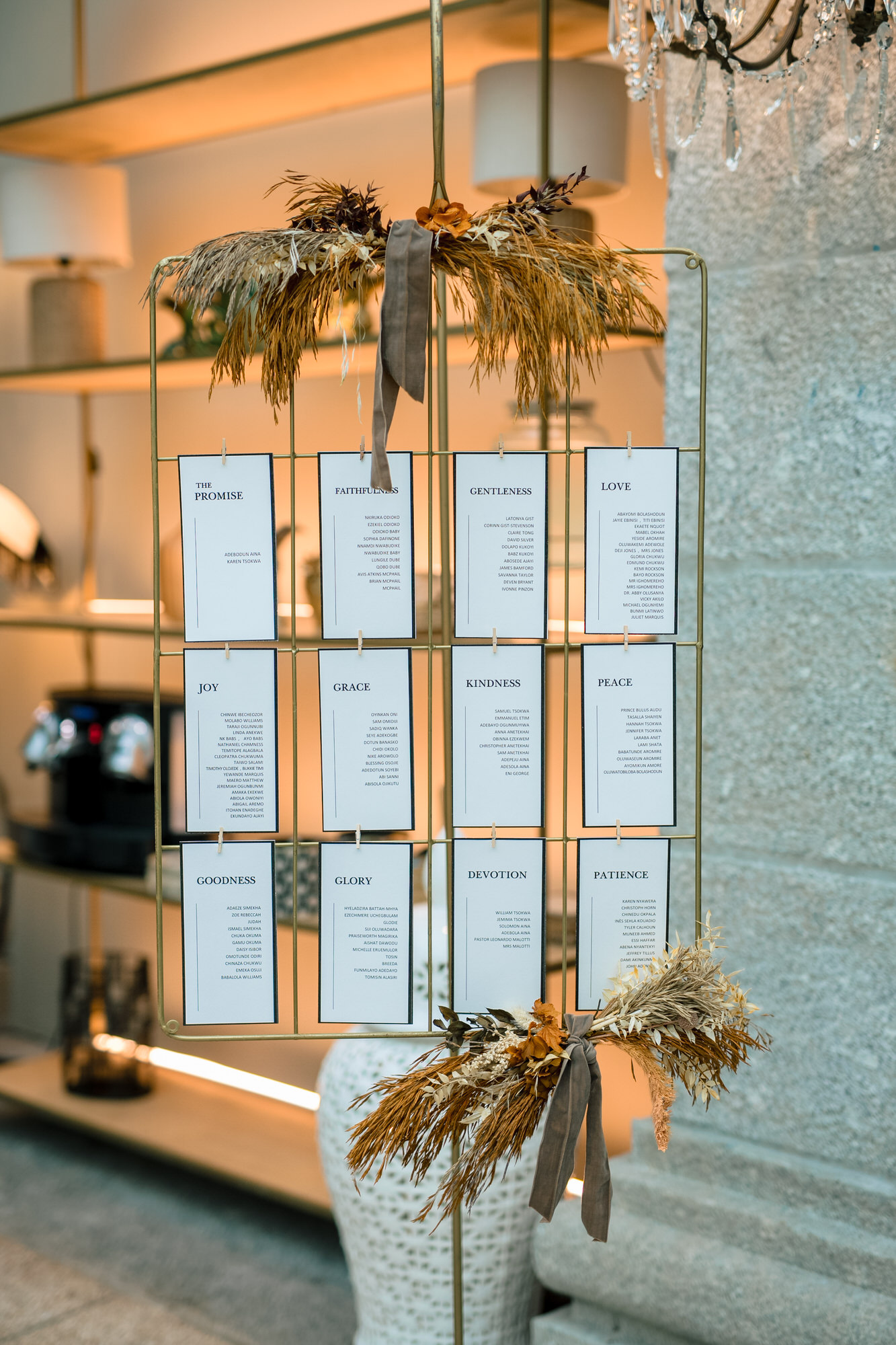 Gold wire display rack holding vertical cards with virtues such as The Promise, Faithfulness, Gentleness, Love, Joy, Grace, Kindness, and Peace, adorned with dried grasses and gray ribbon in a warm-lit interior.