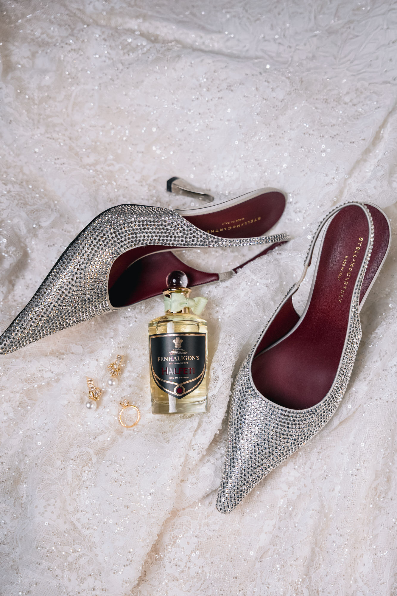 Elegant silver rhinestone heels rest on delicate lace fabric, with a perfume bottle and scattered jewelry nearby