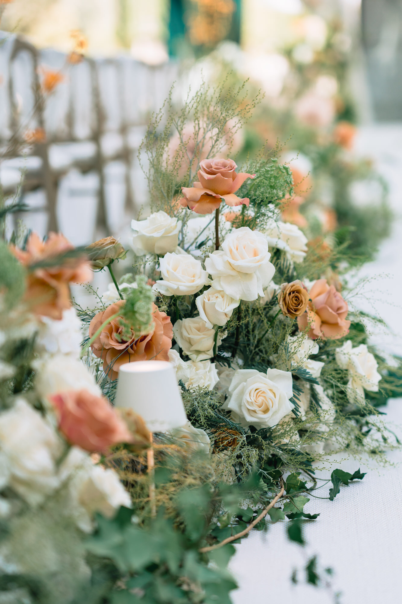 Elegant wedding centerpiece with peach and white roses and greenery on a white tablecloth.