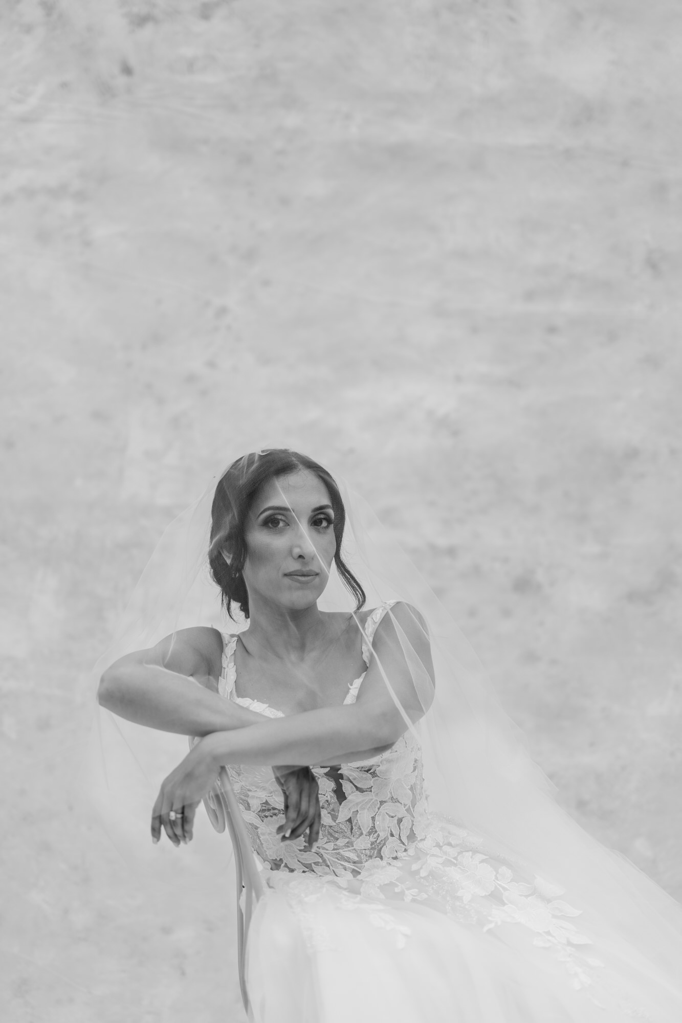 Black-and-white portrait of the bride in her lace gown, arms crossed in a playful pose