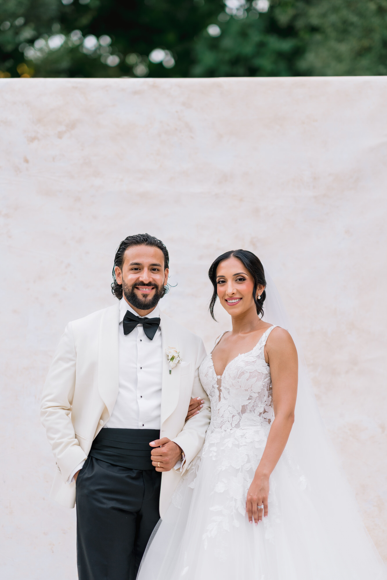 Hana and Andres smiling arm in arm in front of a pale stone wall