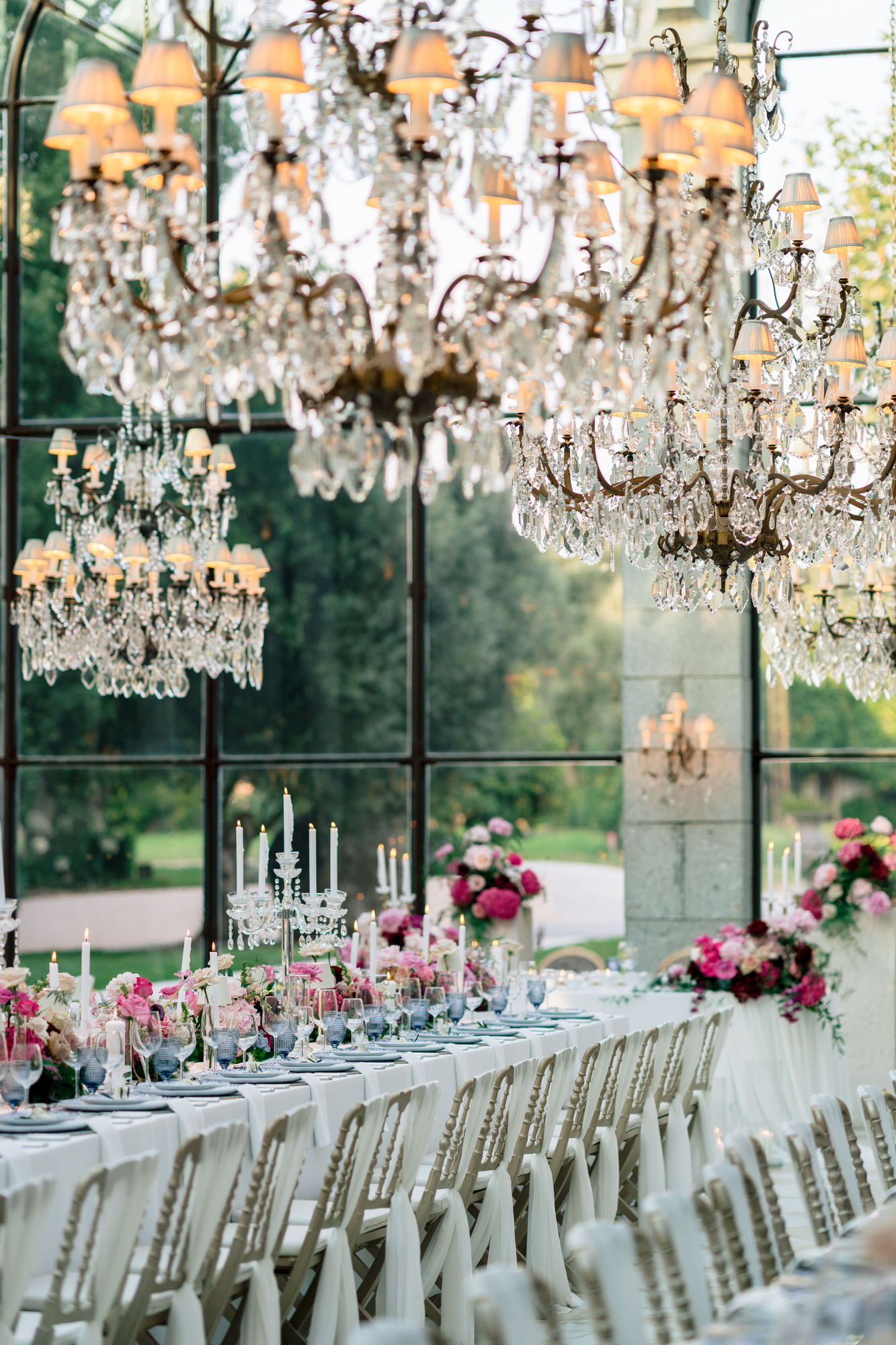 Crystal chandeliers above the long reception table, with the garden visible through the glass wall