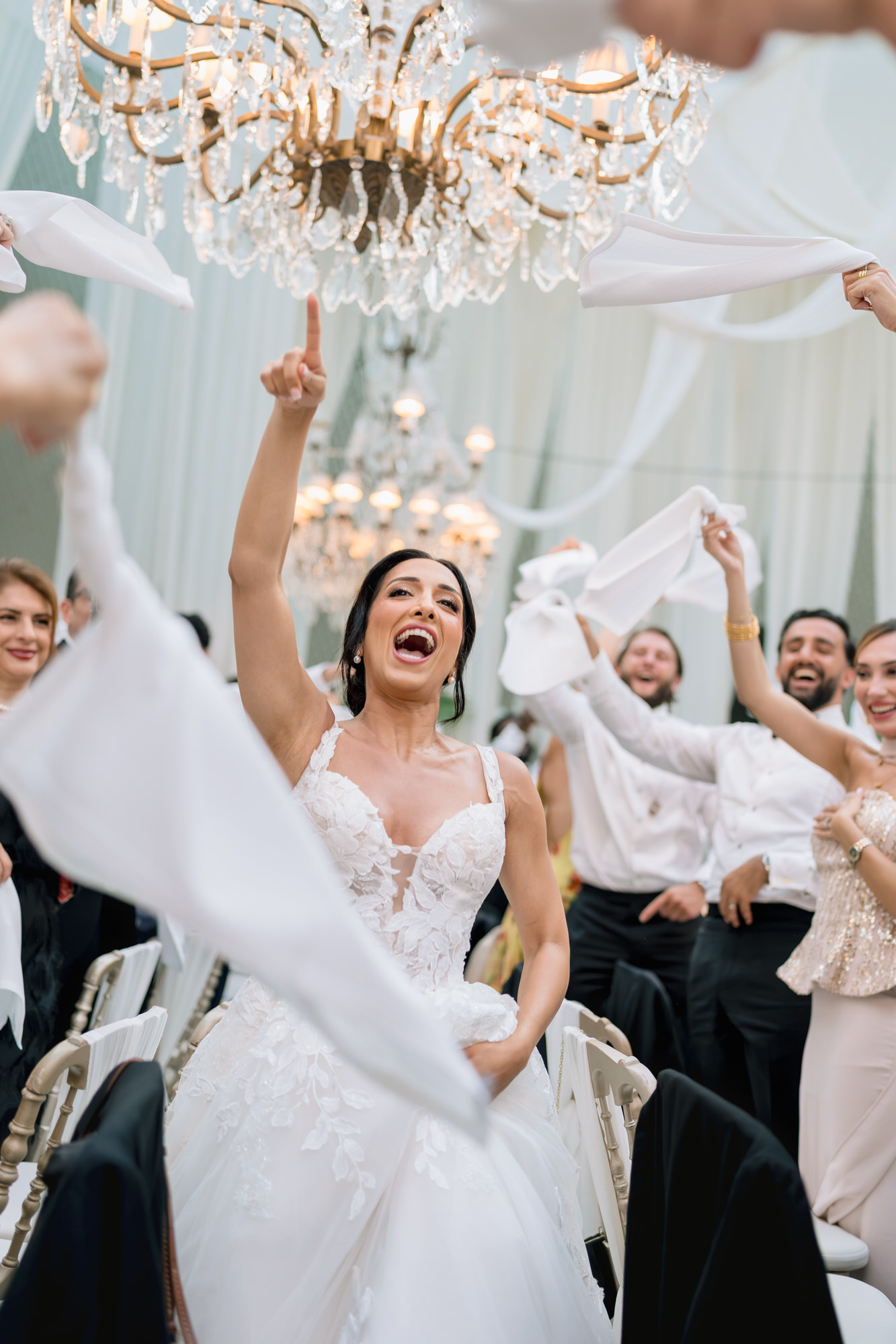 The bride dancing with her arm raised as guests wave white napkins around her