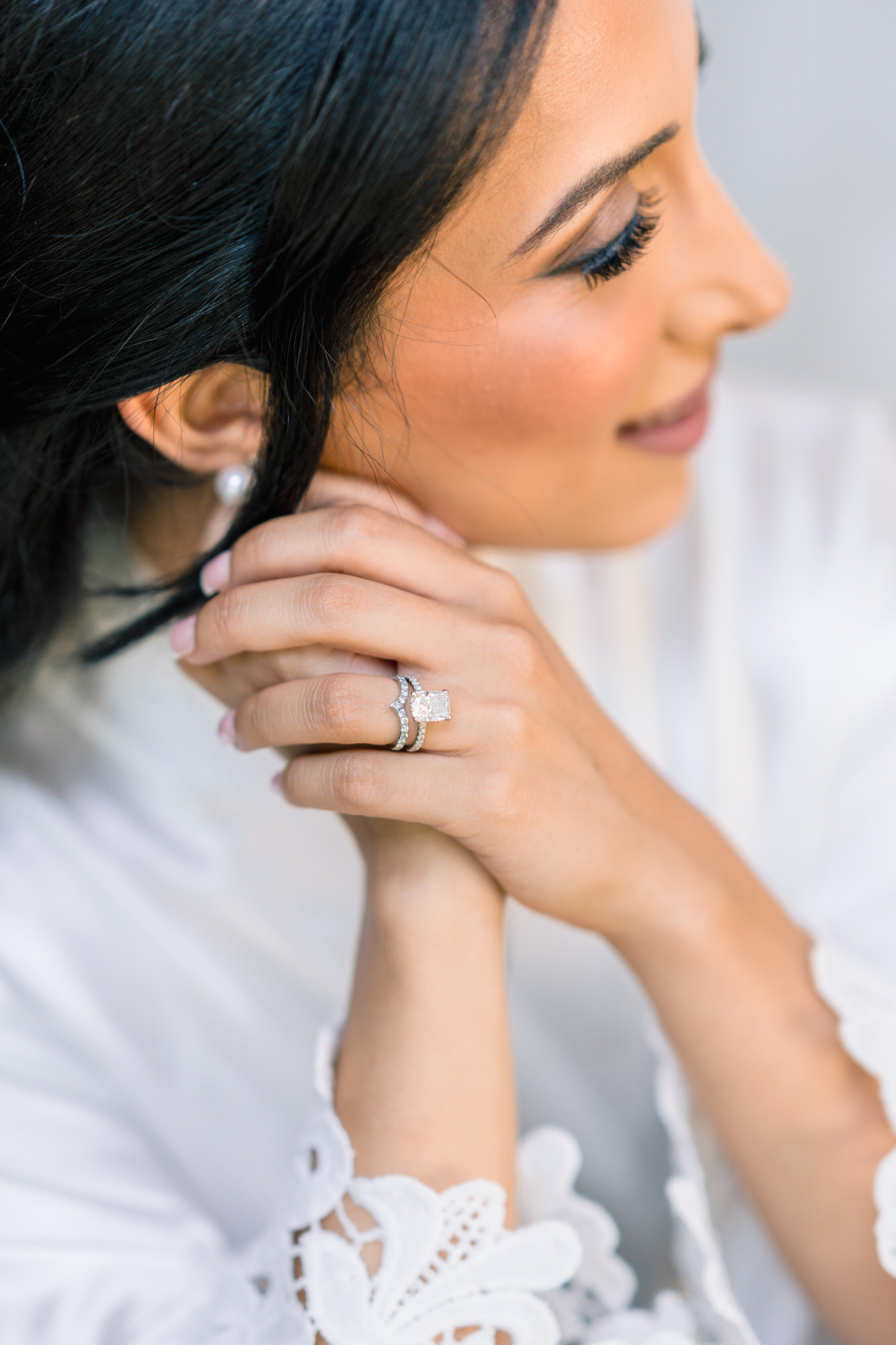 Profile of the bride with her hand at her face, a diamond ring and a lace sleeve visible while her hair is styled