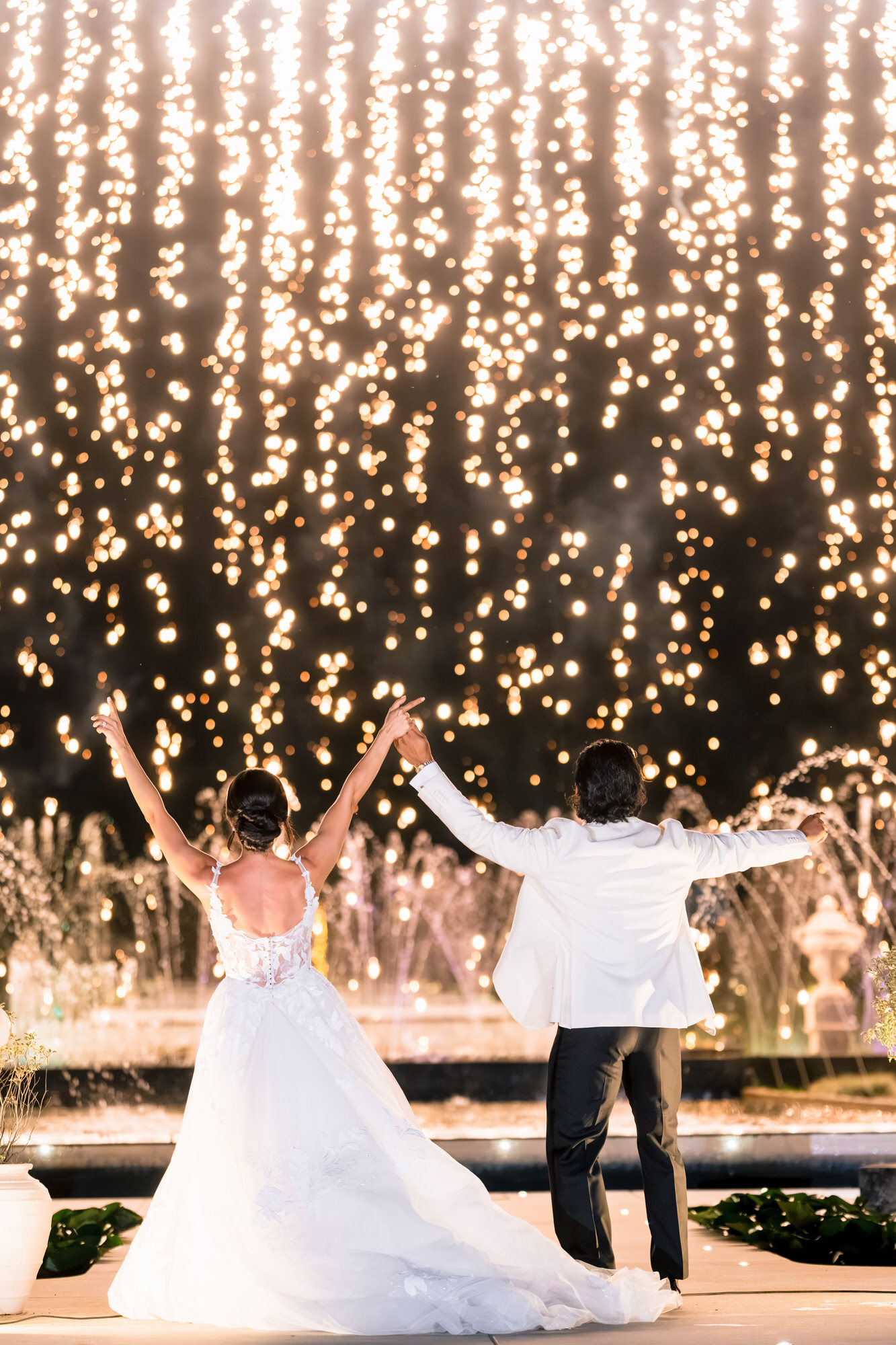 Hana and Andres dancing with raised arms in front of a curtain of fairy lights