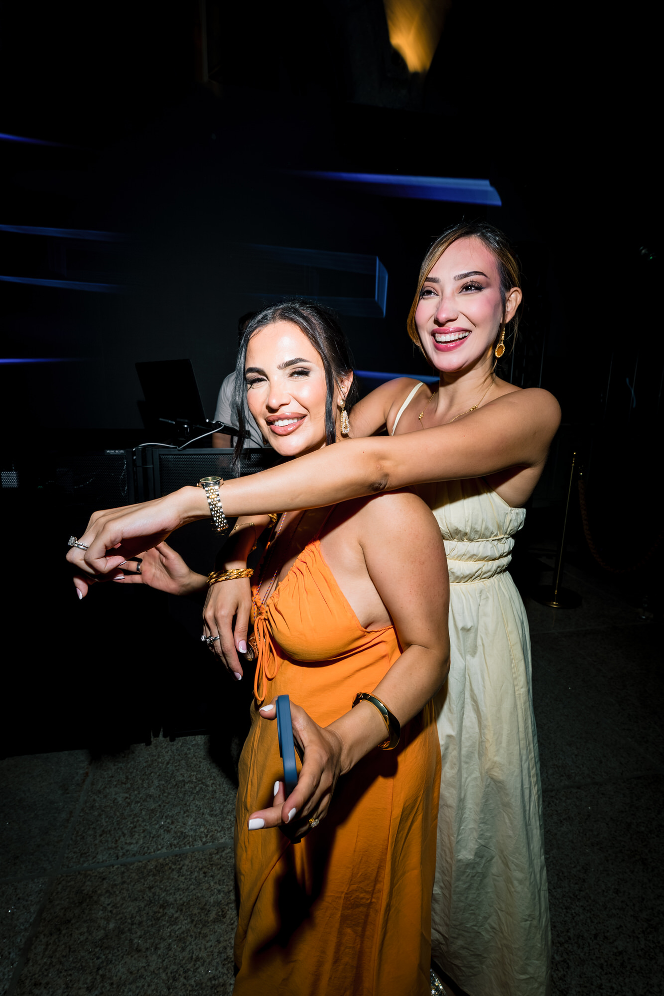 Two guests embracing and laughing on the dance floor, one in an orange gown