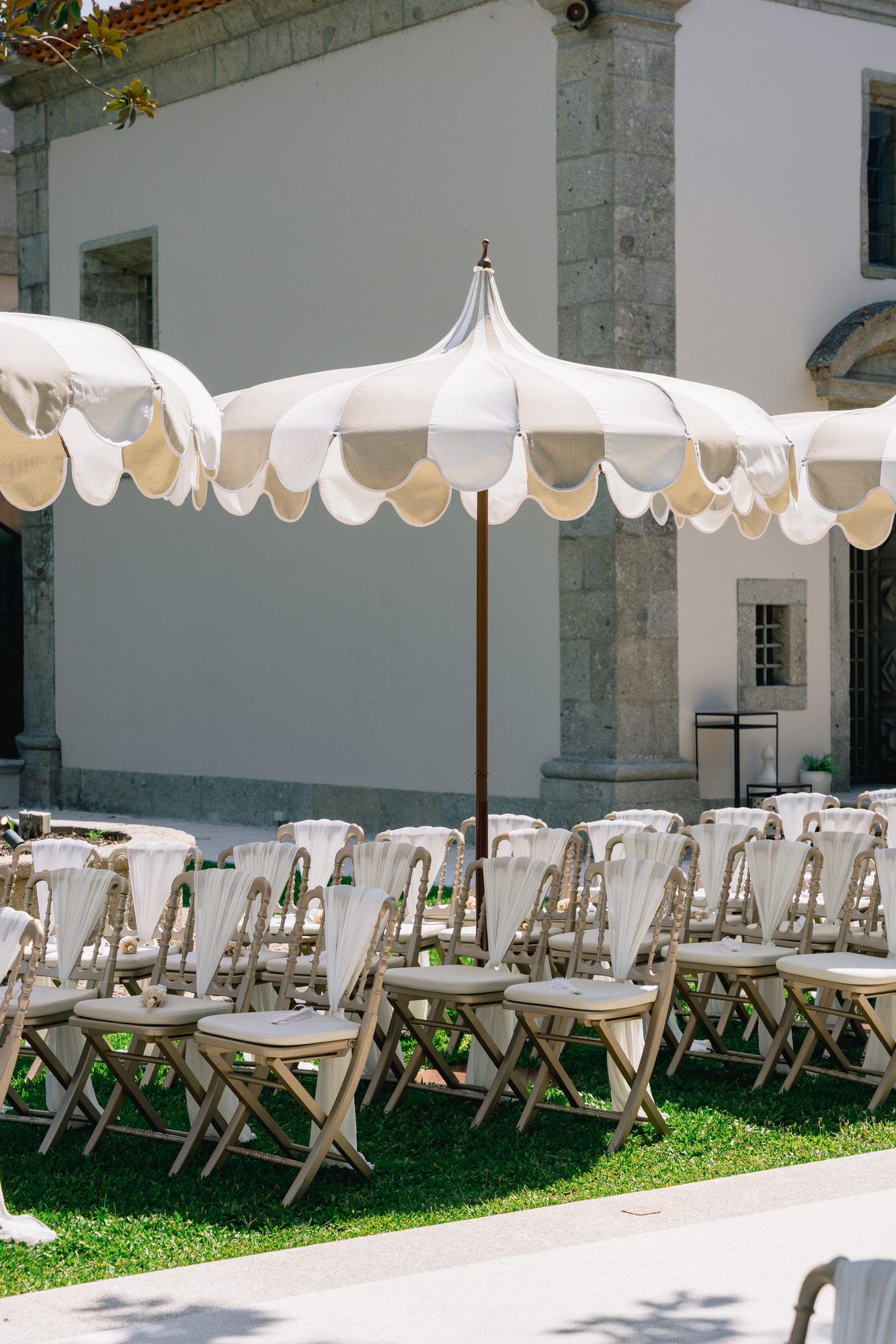 Folding chairs under a white scalloped parasol on the lawn, prepared for the garden ceremony at Solar da Levada
