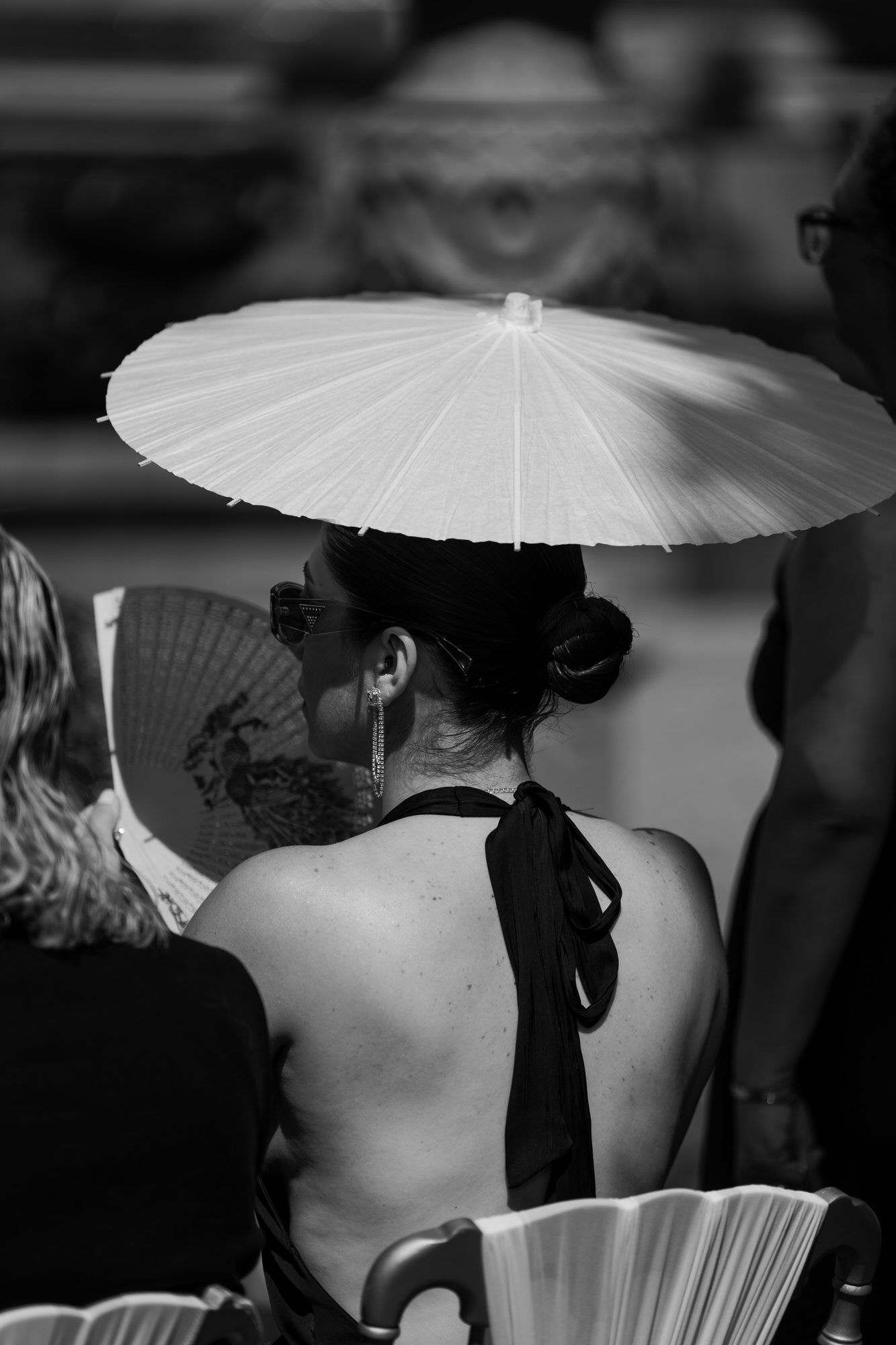 Black-and-white image of a guest seen from behind in a halter top, holding a fan beneath a white parasol