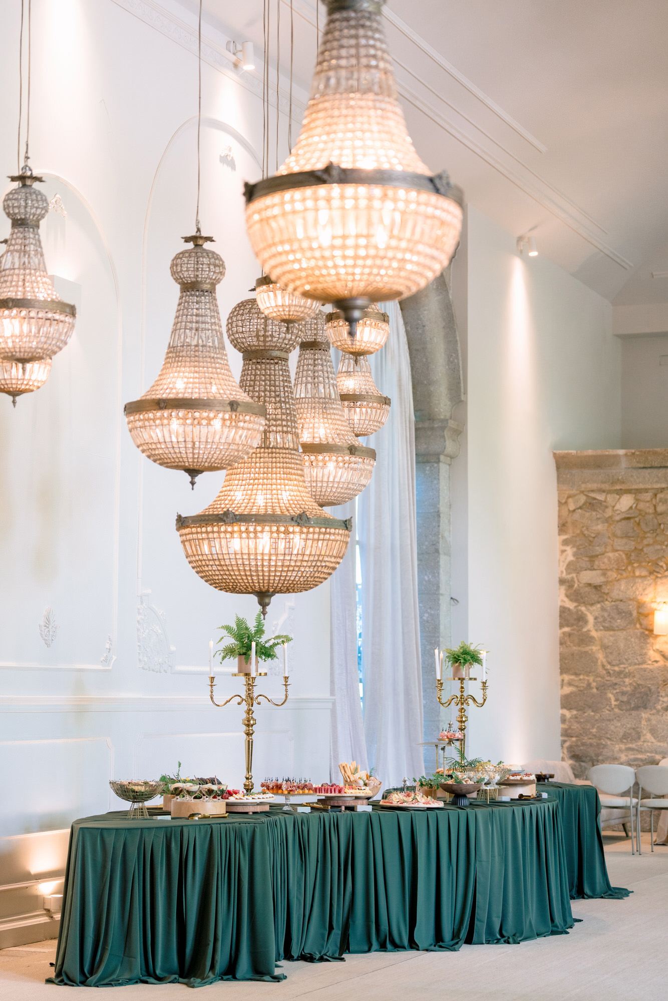A dessert table with an emerald-green cloth beneath hanging crystal chandeliers