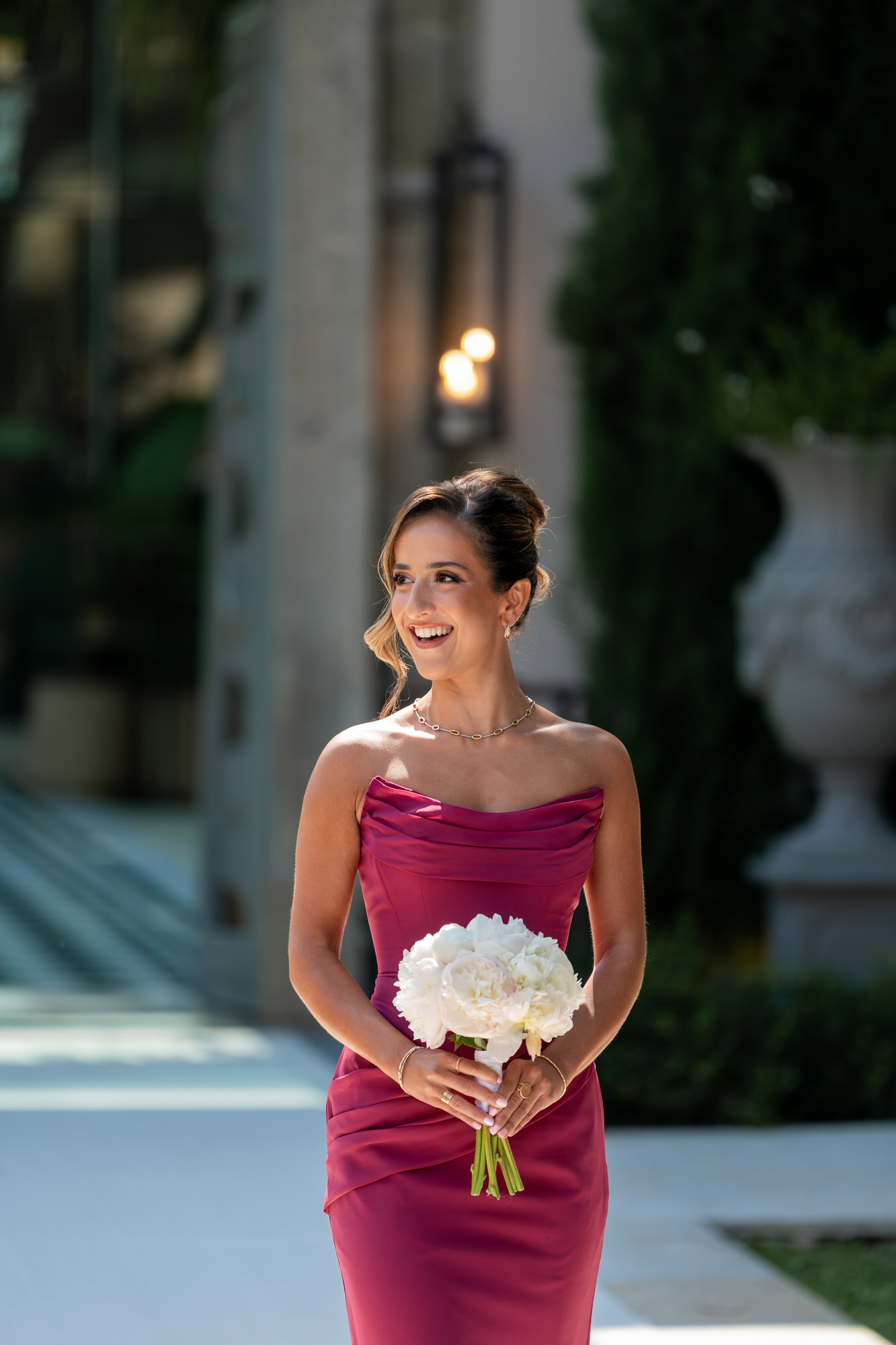 A bridesmaid in a berry-coloured strapless dress holding a white bouquet as she walks to the ceremony