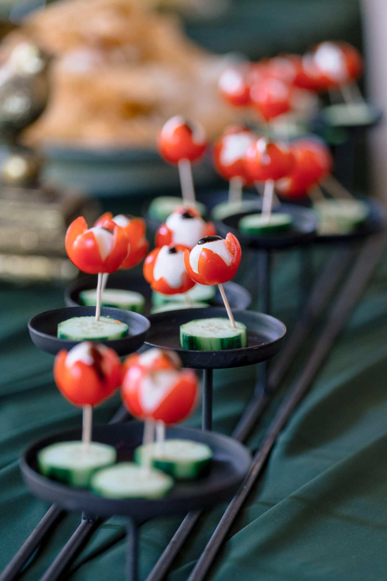 Red cherry-tomato canapés on skewers, served on a dark green plate