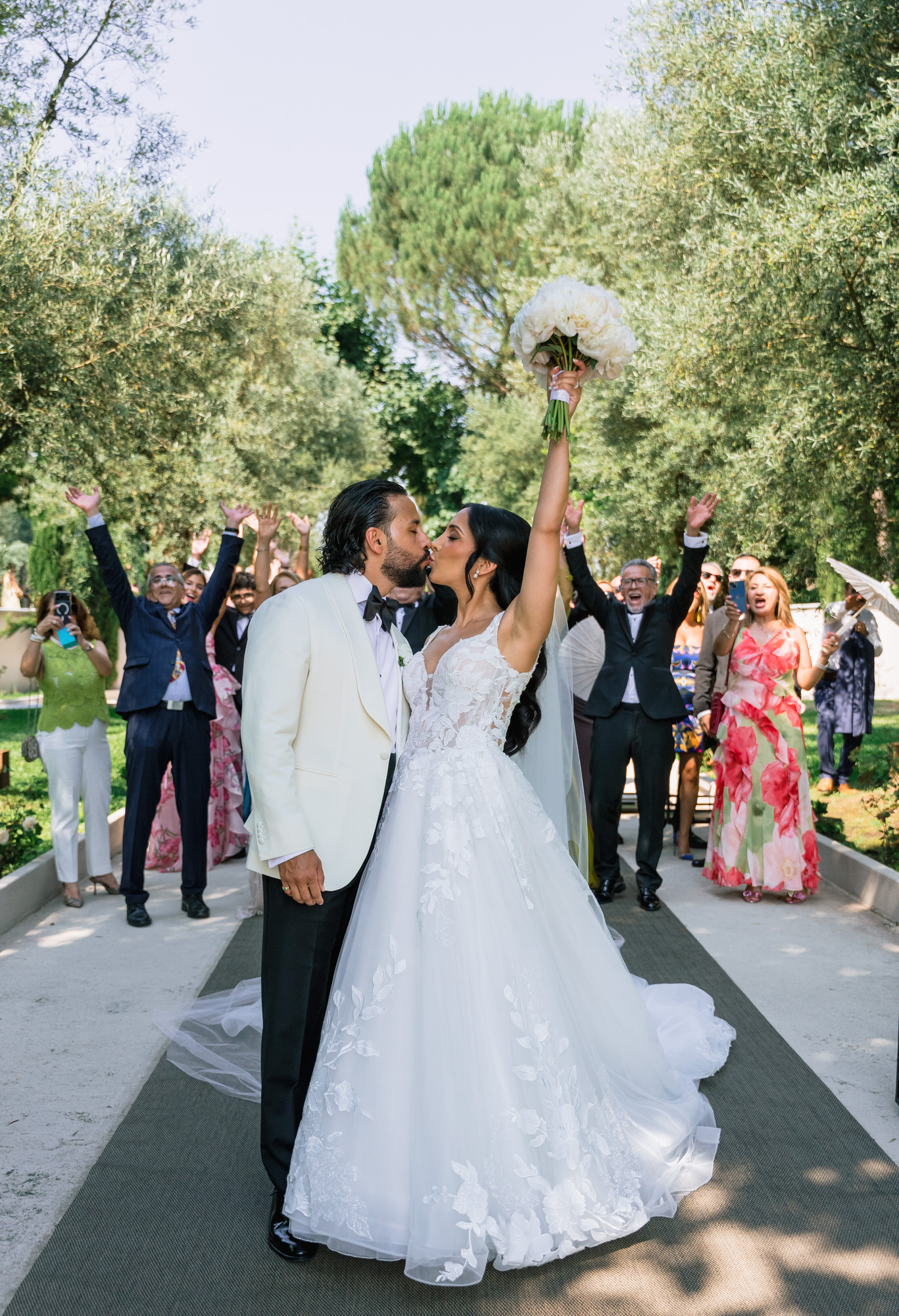 The couple walking down the path as guests cheer, the bride raising her bouquet and the groom his fist