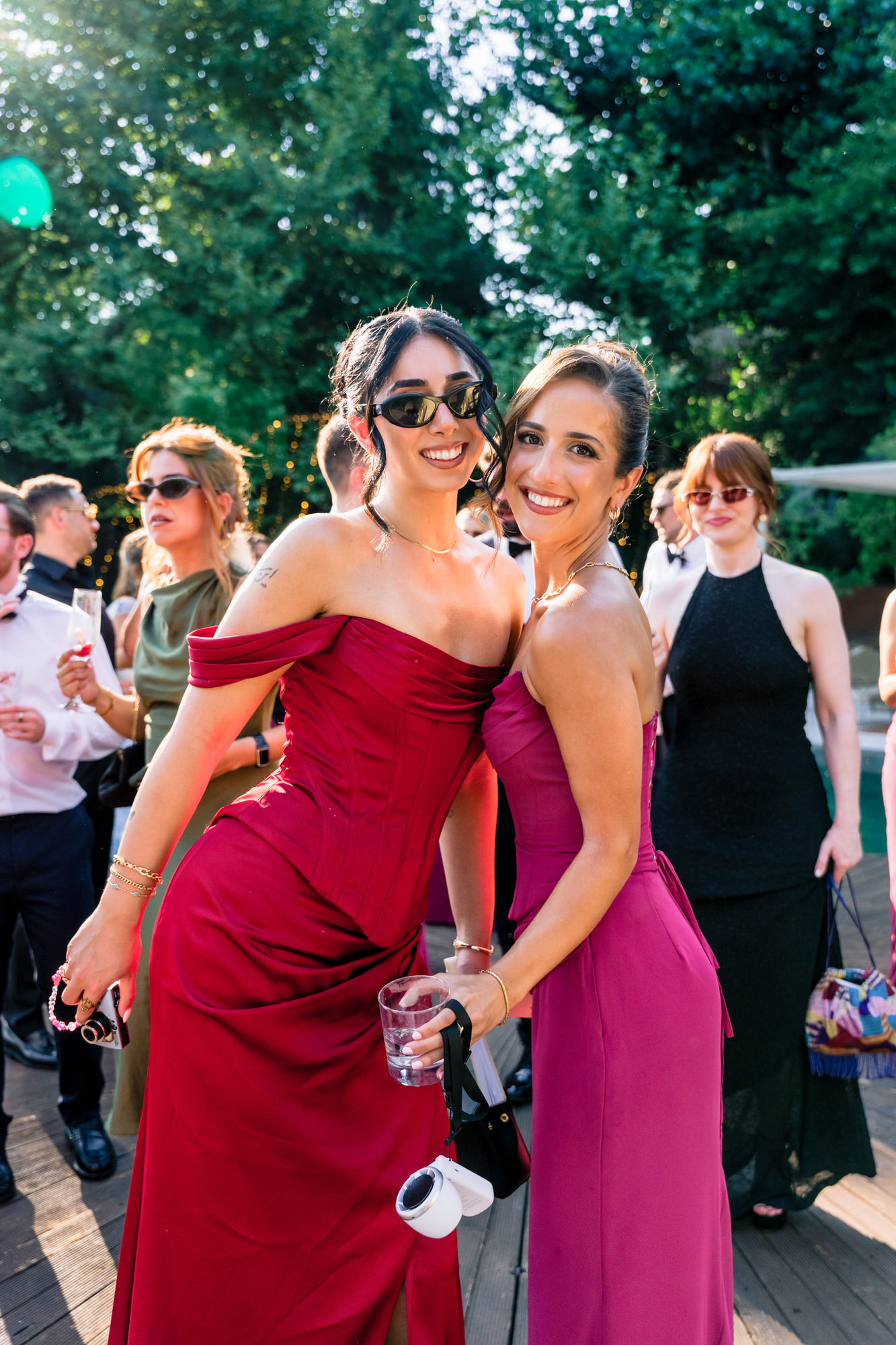Two guests in red and fuchsia dresses posing together with sunglasses by the pool