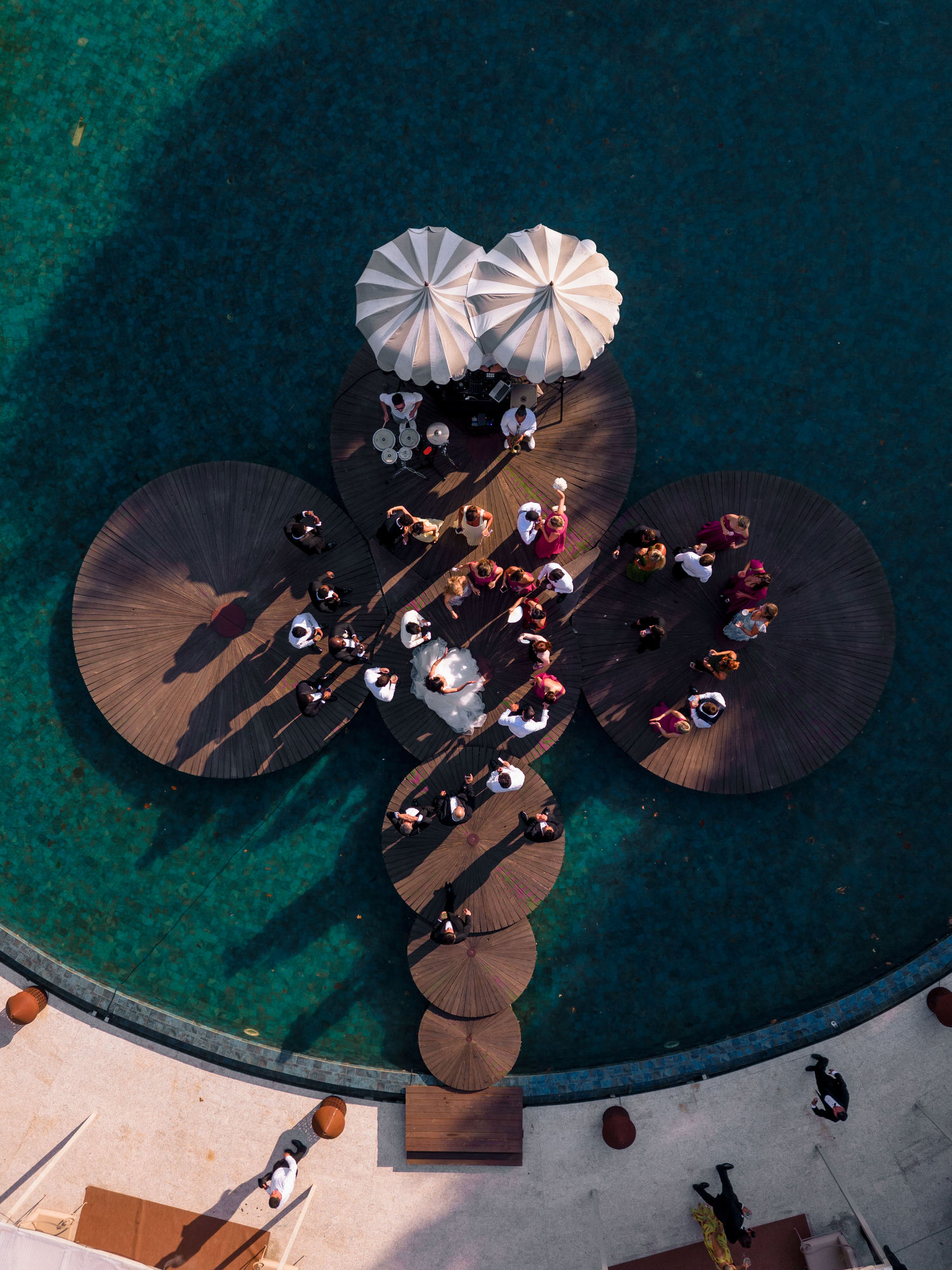 Overhead view of white parasols and lounge seating beside a deep green pool