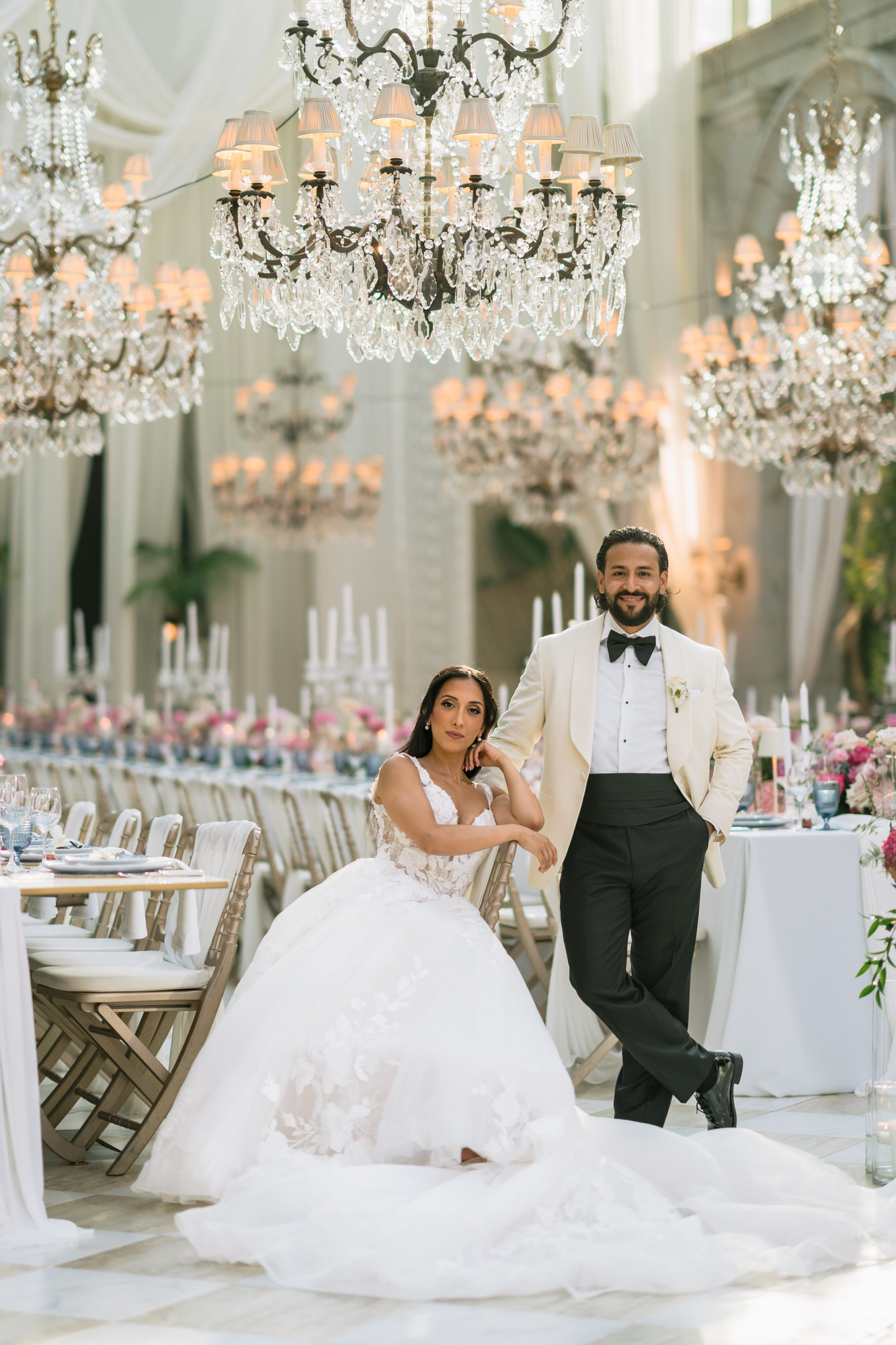Hana seated in her voluminous gown beside Andres in a white dinner jacket, in a chandelier-lit hall at Solar da Levada