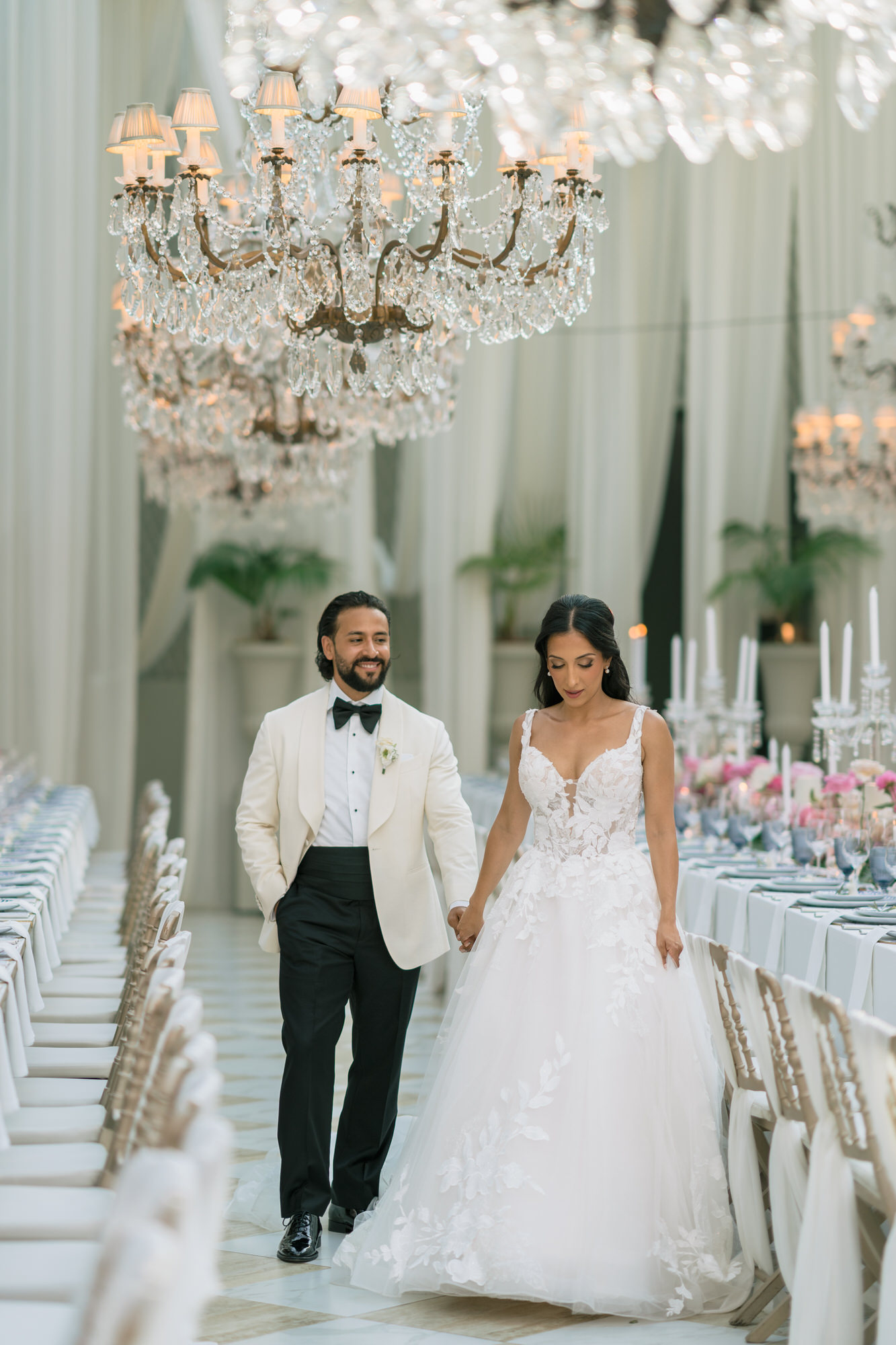 Hana and Andres holding hands in the glass-roofed reception hall at Solar da Levada, chandeliers above long tables