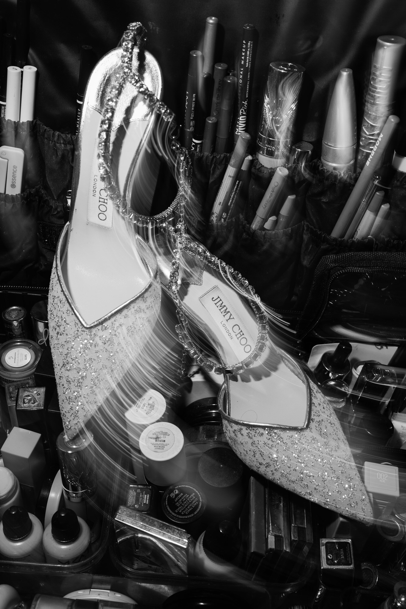 Black-and-white detail of the bride’s sparkling heels resting among make-up brushes