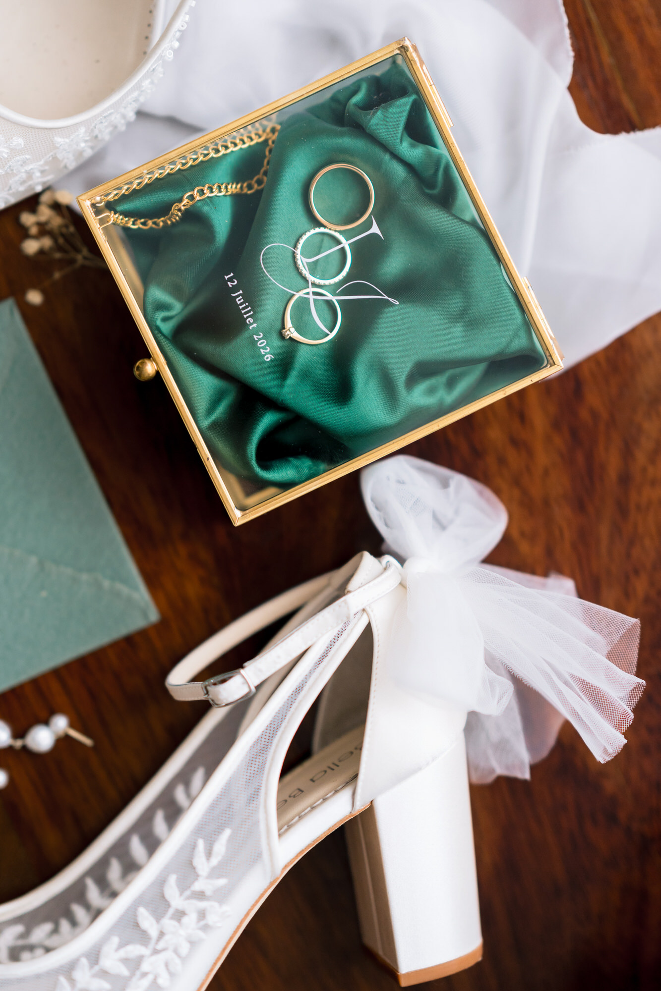 Flat lay of a green jewellery box with the rings beside the bride’s lace heels with a tulle bow