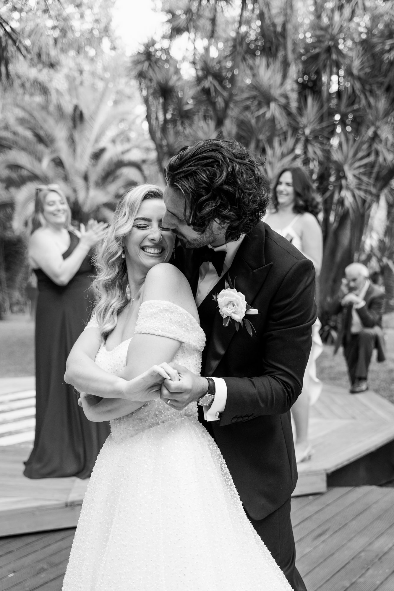 Black-and-white image of the couple embracing, the groom kissing the bride’s temple