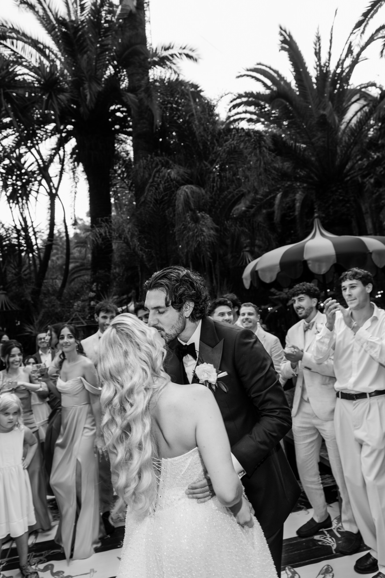 Black-and-white image of the couple kissing as guests cheer around them
