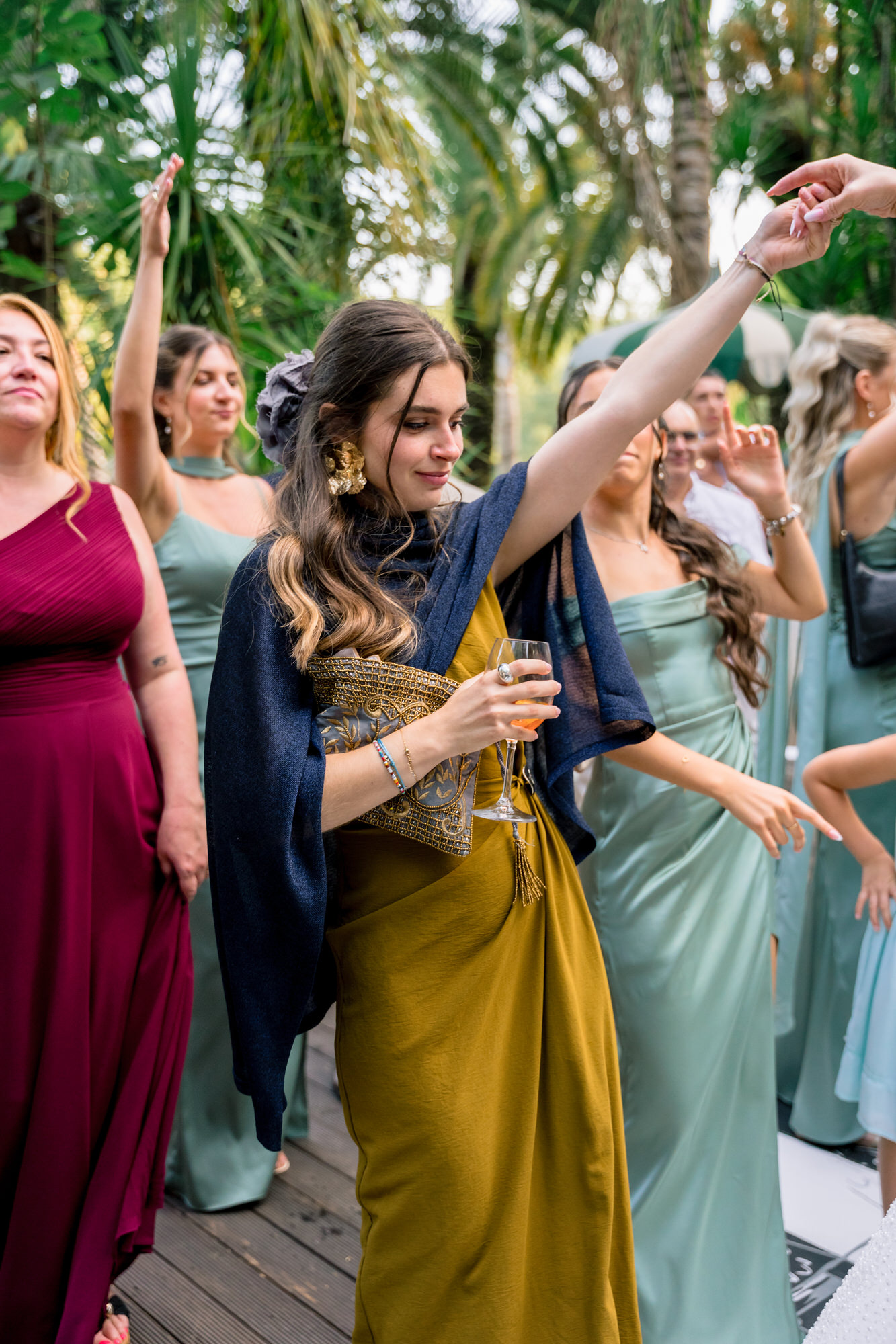 Female guests in burgundy, sage and mustard dresses dancing with their arms raised