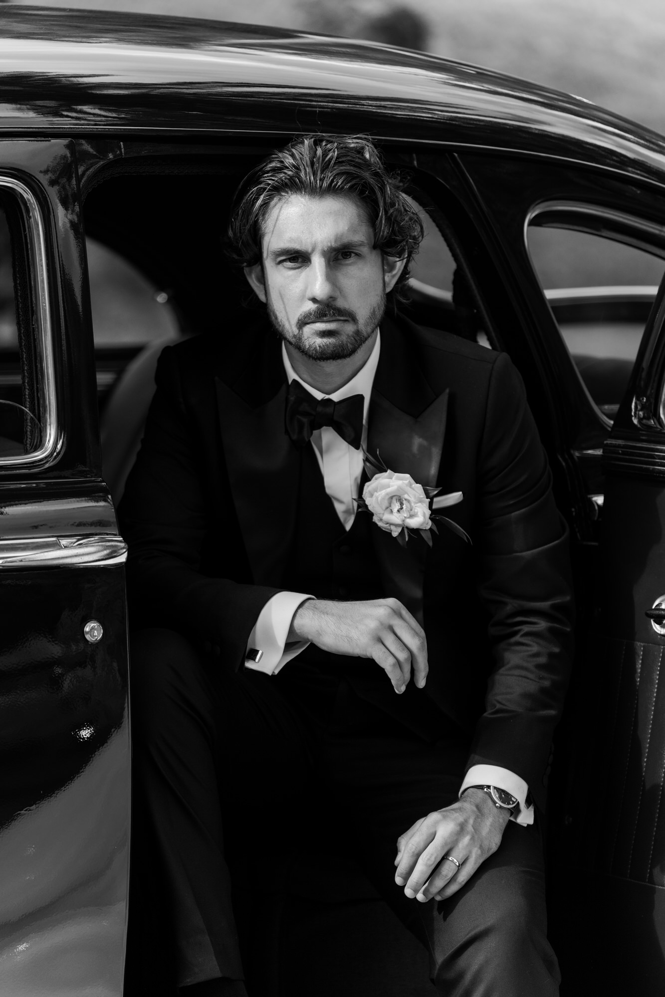 Black-and-white portrait of the groom seated in the back of a classic black car