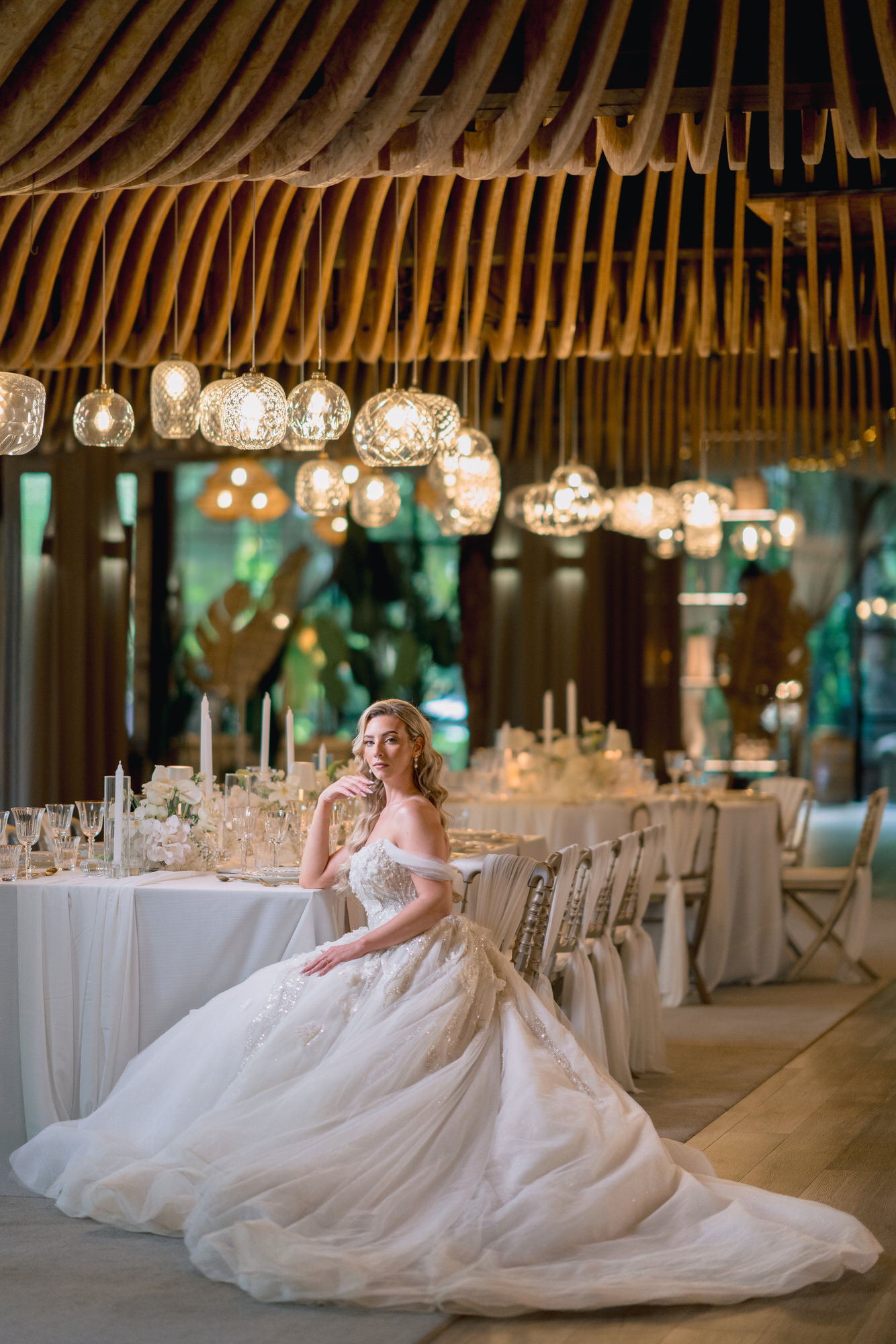 The bride seated in her gown in the reception hall, tables set behind her under the wooden ceiling