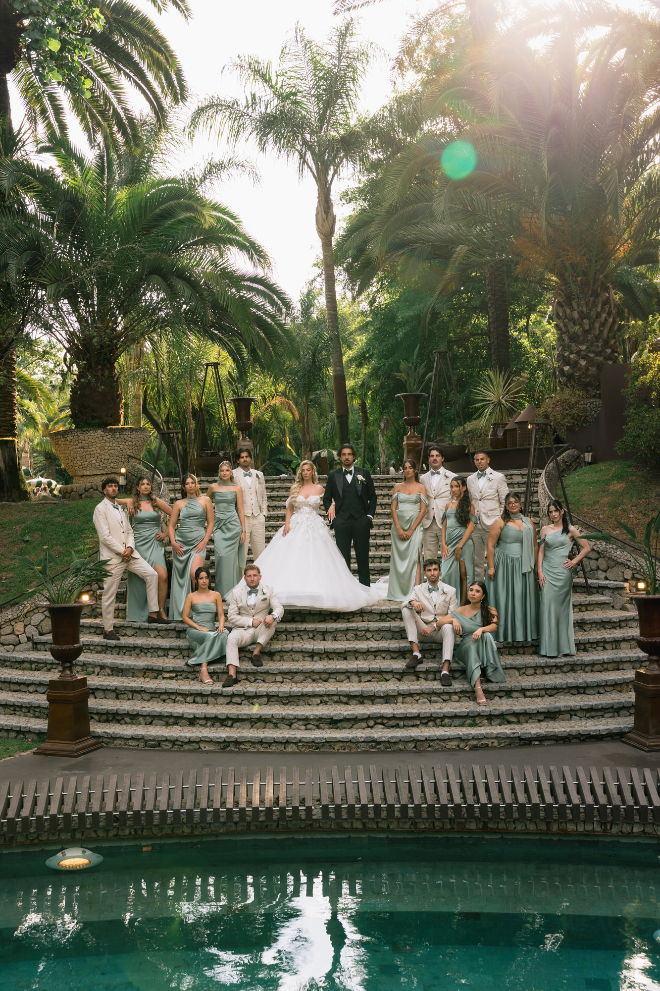 The wedding party on the garden steps beside the pool, bridesmaids in sage-green dresses