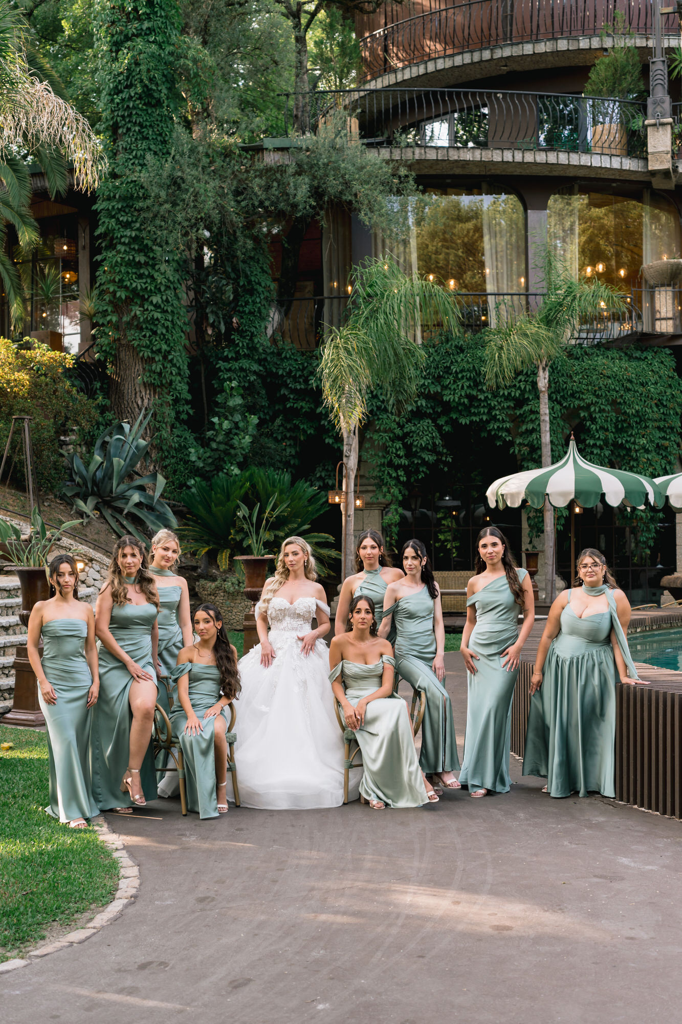 The bride surrounded by her bridesmaids in sage-green dresses on the garden path
