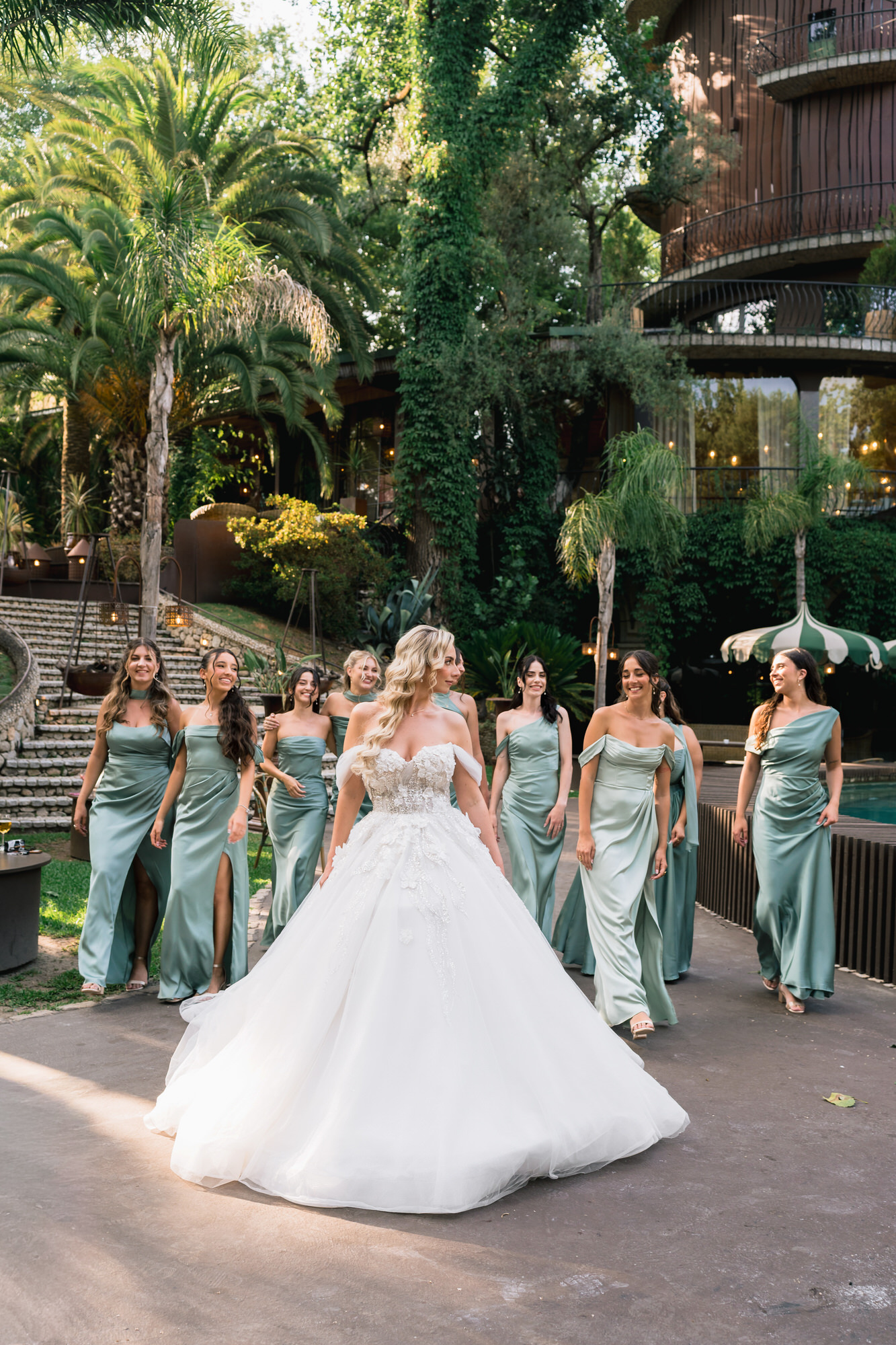 The bride walking towards the camera with her bridesmaids in sage-green dresses behind her
