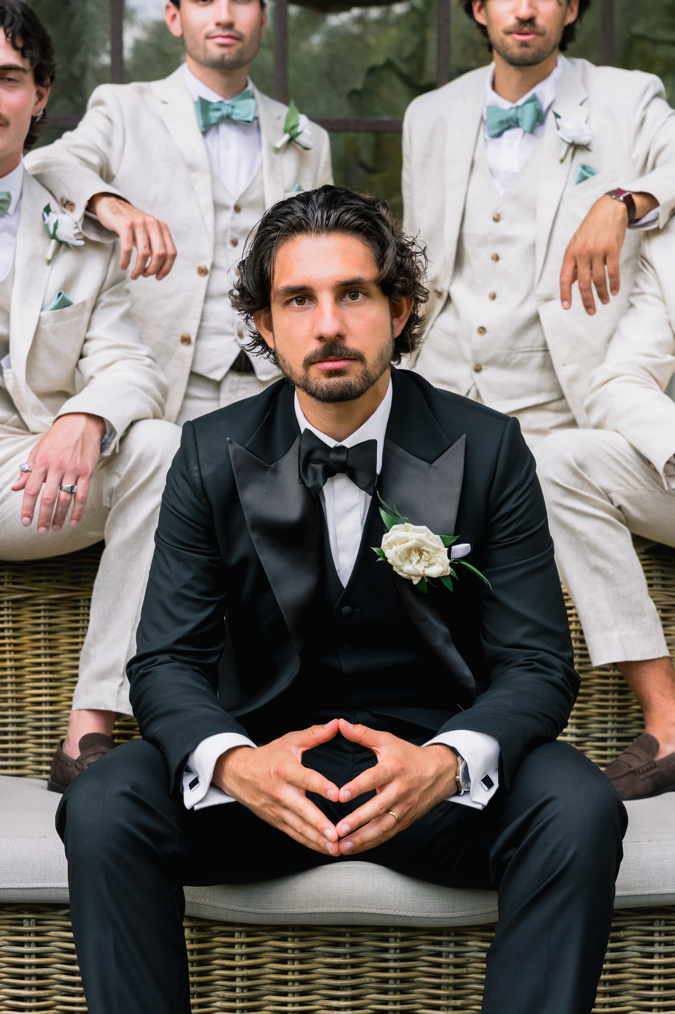 Close-up of the groom with his hands together, groomsmen in cream suits behind him