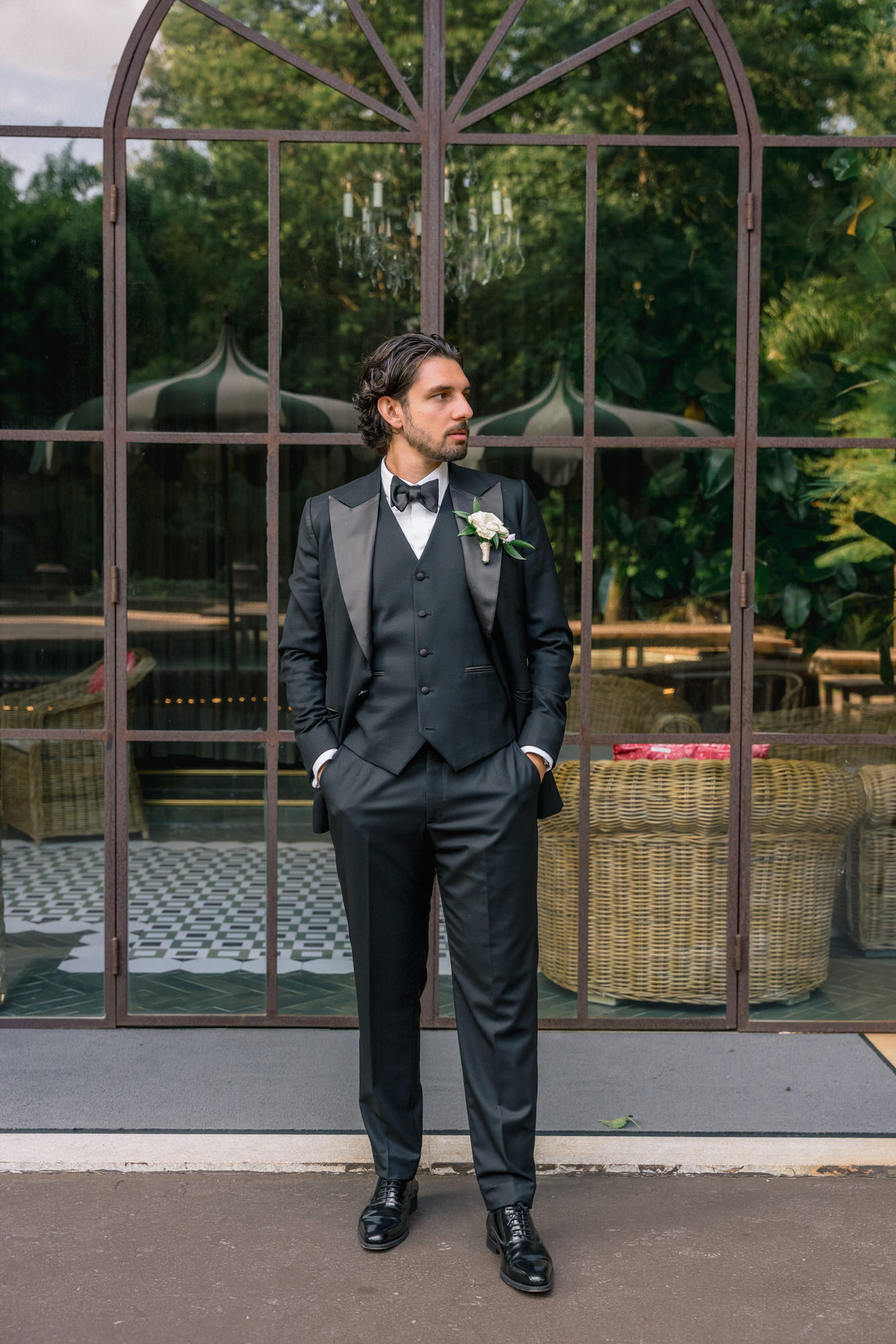 The groom in a black tuxedo standing in front of dark glass doors and a checkered floor