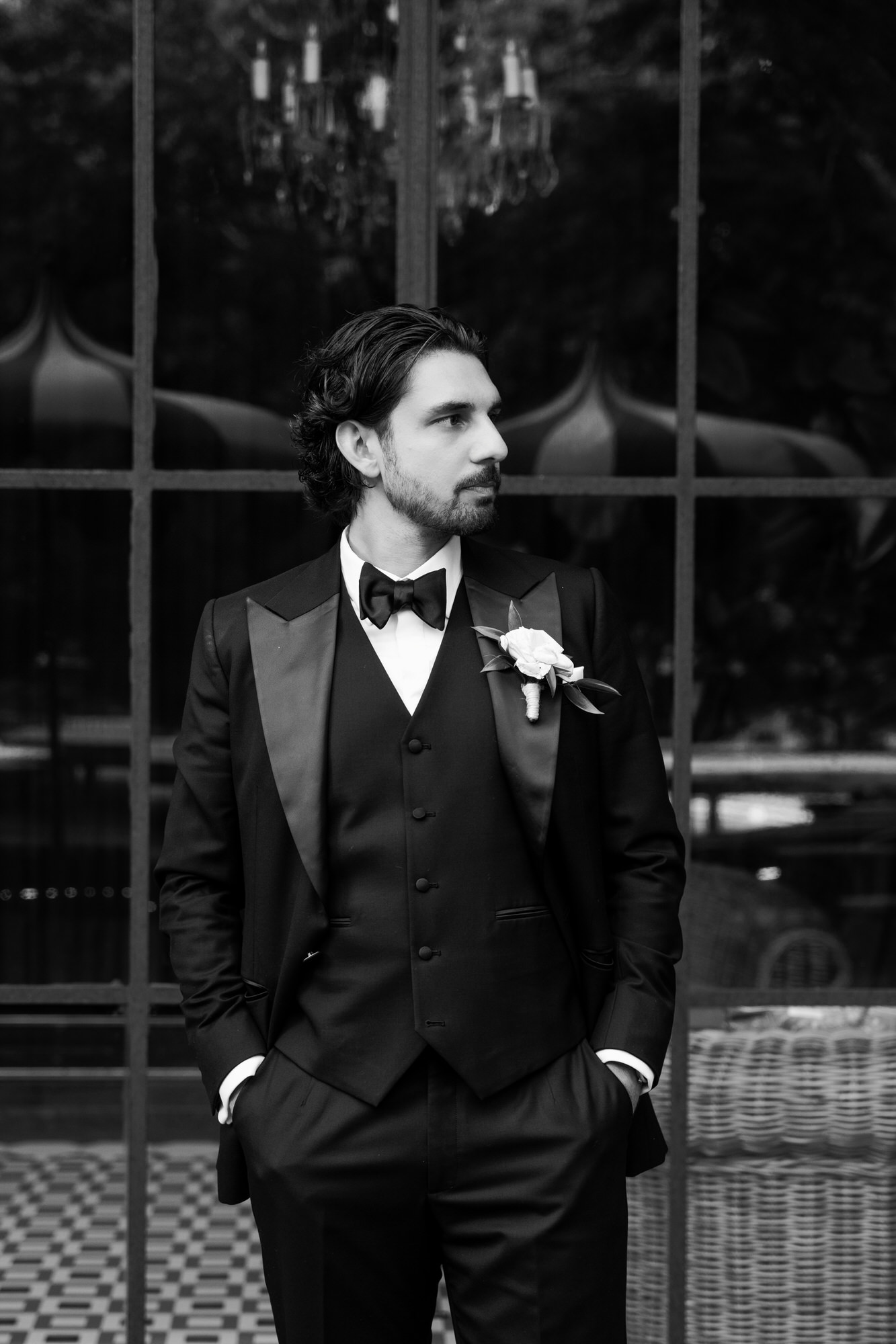 Black-and-white portrait of the groom in a three-piece tuxedo, hands in his pockets