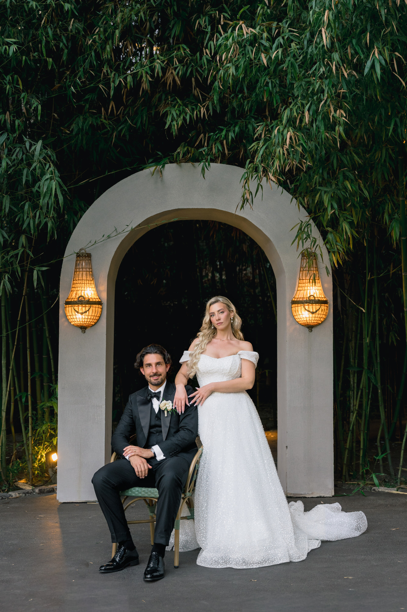 Jessica and Luca seated together before a stone archway with lanterns in the gardens of Quinta Lago dos Cisnes