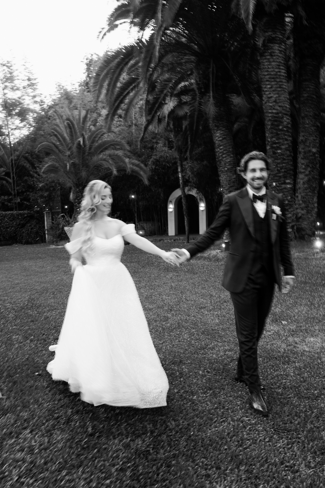 Black-and-white image of the couple walking hand in hand across the lawn
