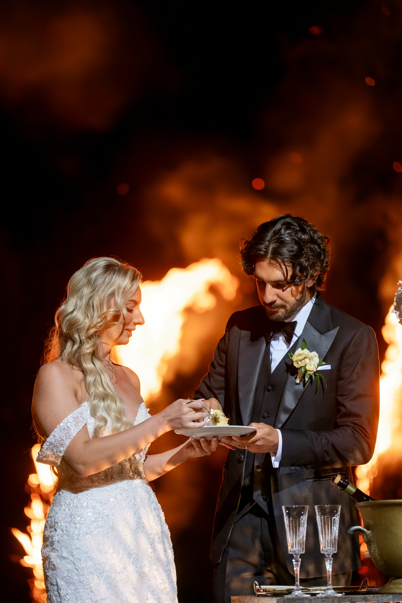 The couple raising a toast at night as flames rise behind them