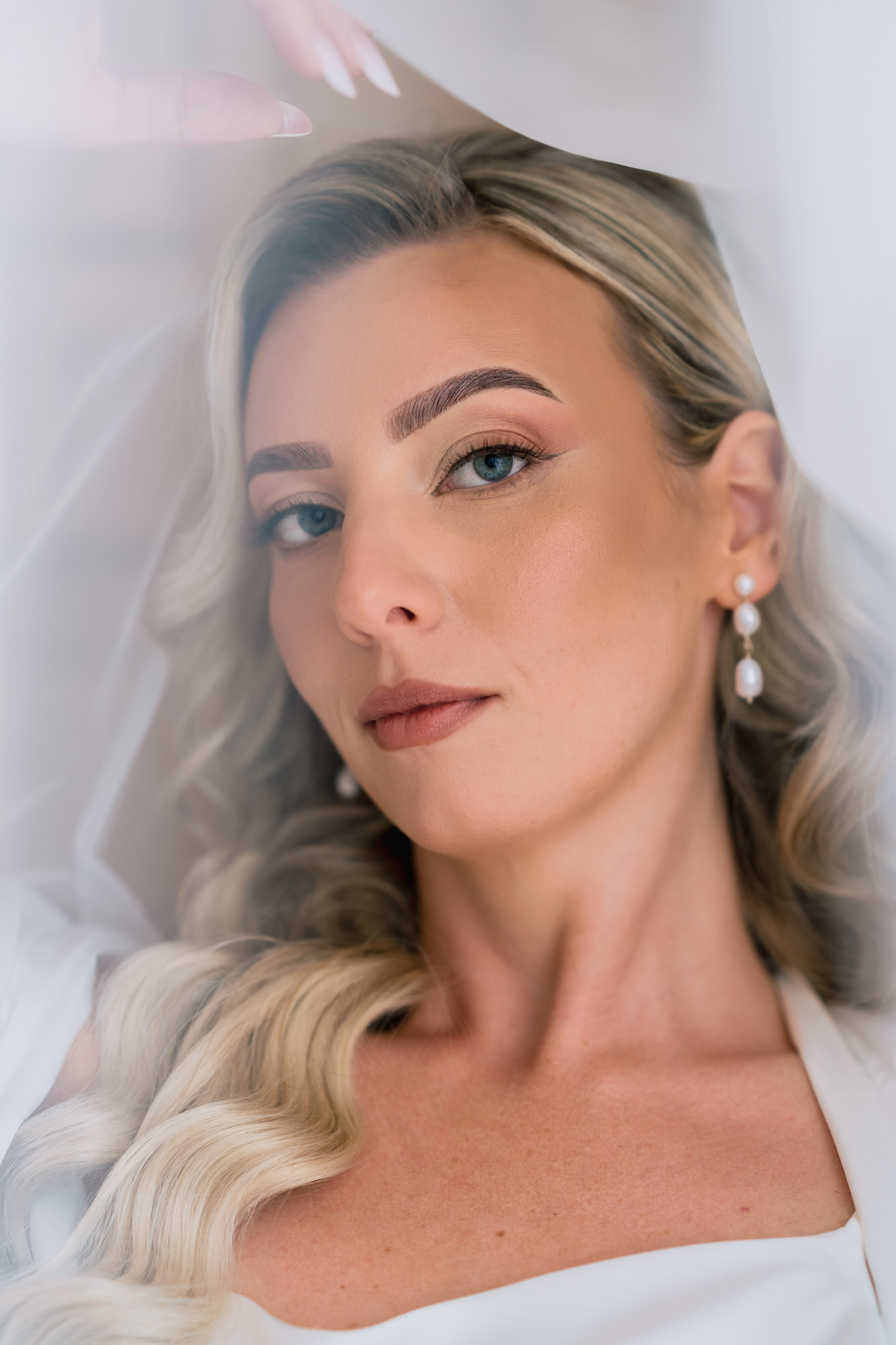 The bride lying back with her veil across her face, pearl earrings catching the light