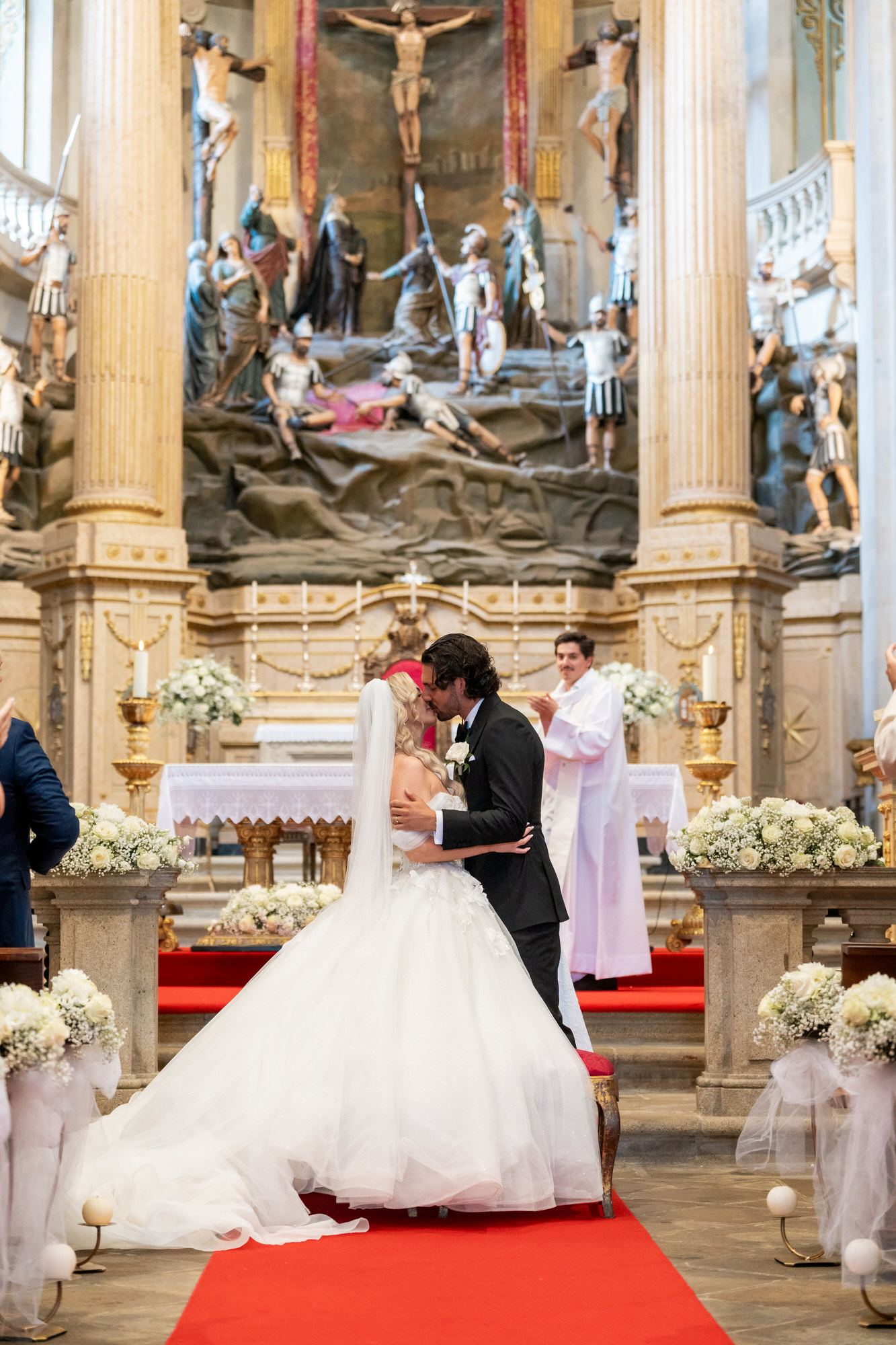 The couple kissing at the altar before a gilded retable, the red carpet running behind them