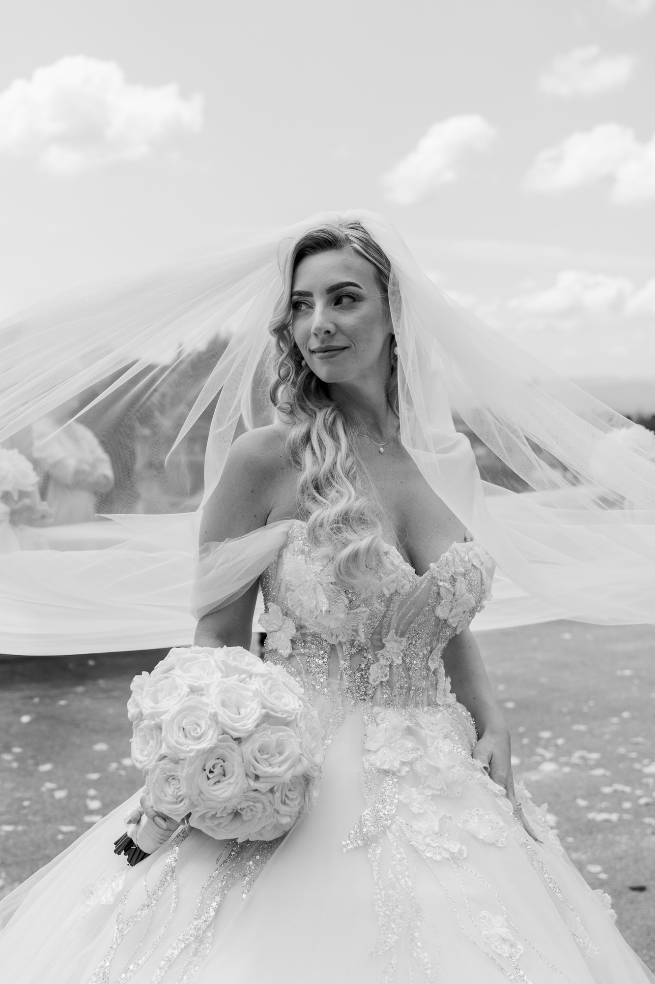 Black-and-white portrait of the bride in her veil, holding a white rose bouquet