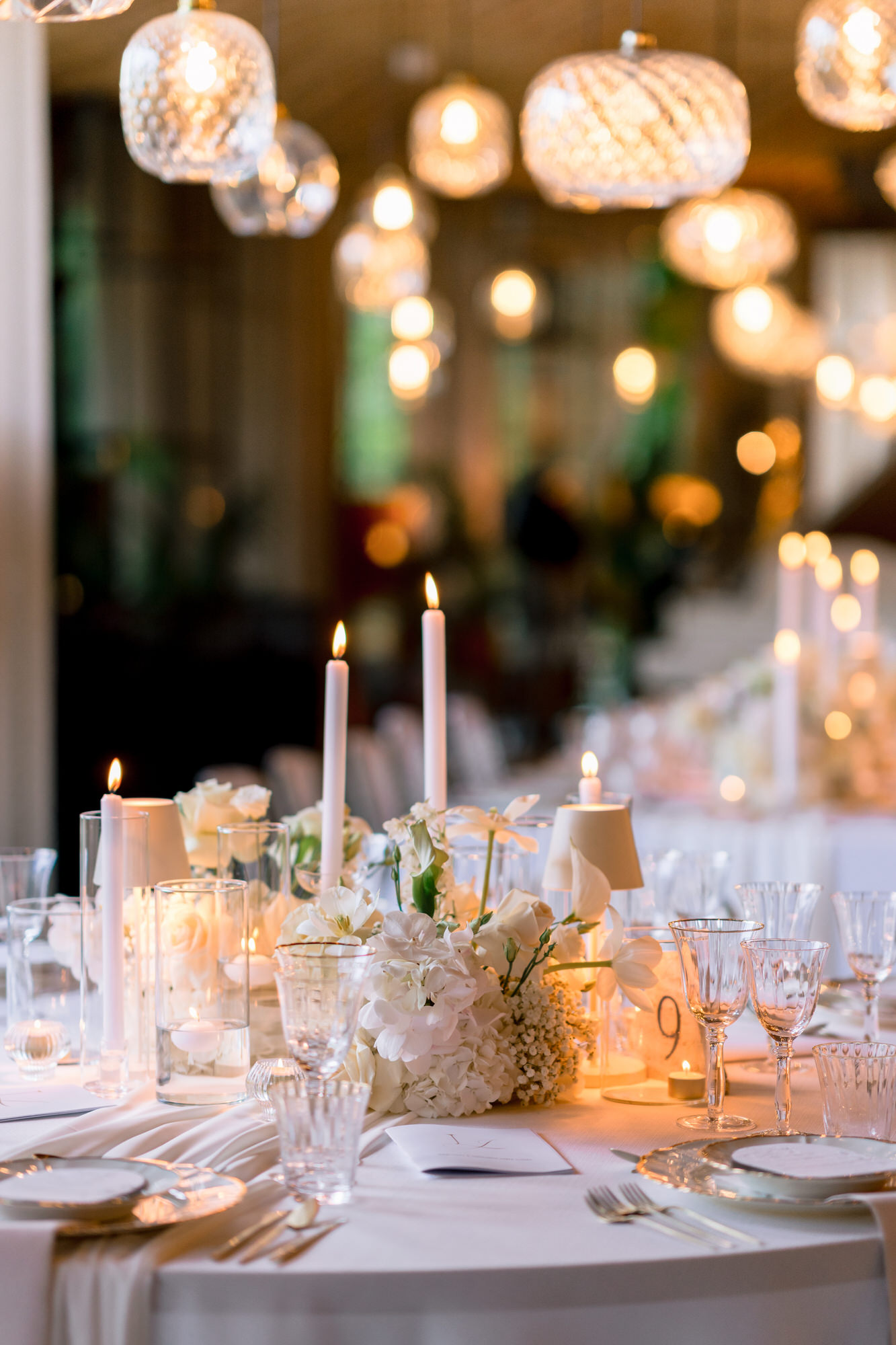 A dinner table with candles, crystal glassware and warm light from the chandeliers