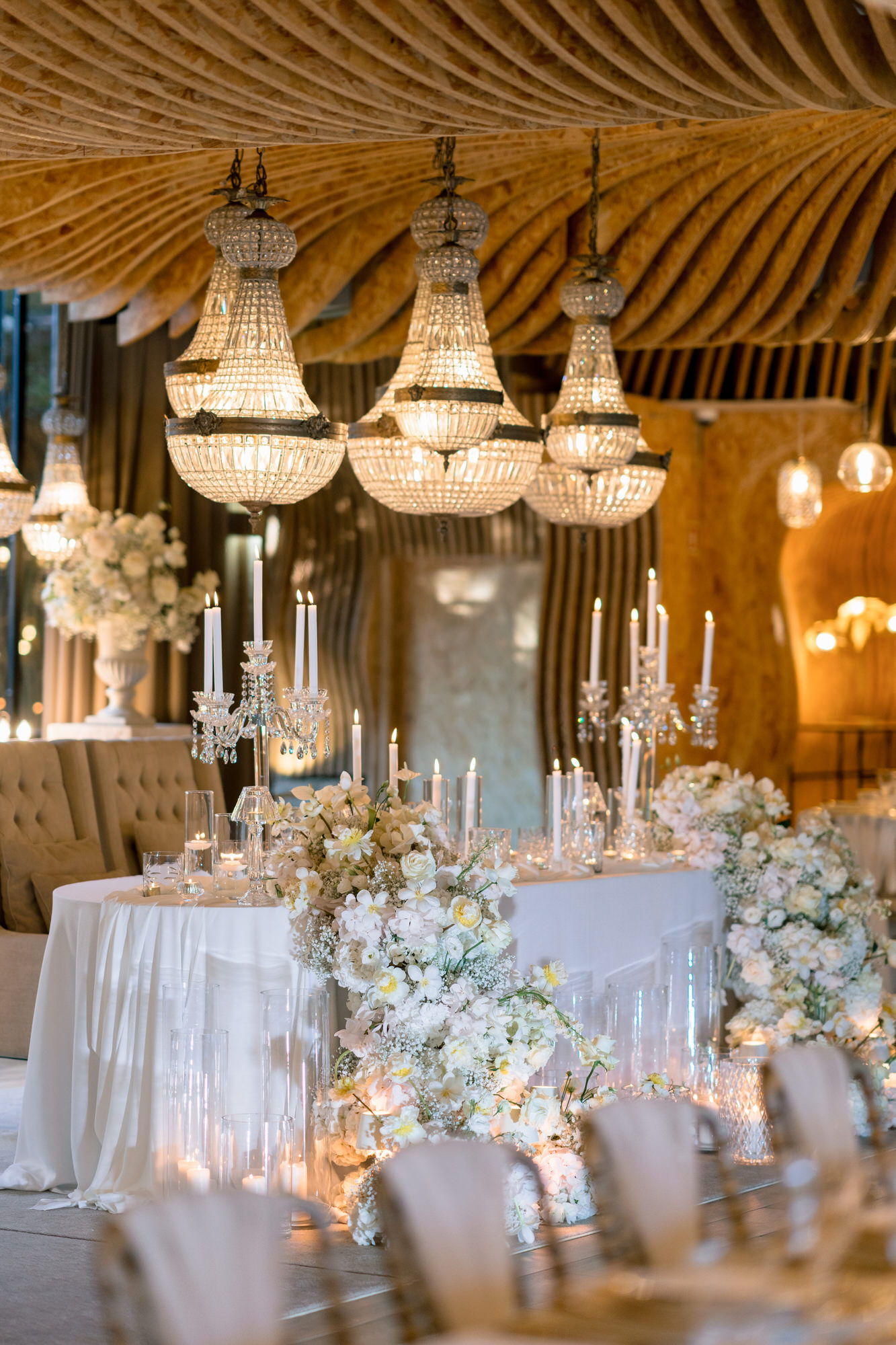 Chandeliers hanging beneath a wooden canopy above a table dressed with white flowers