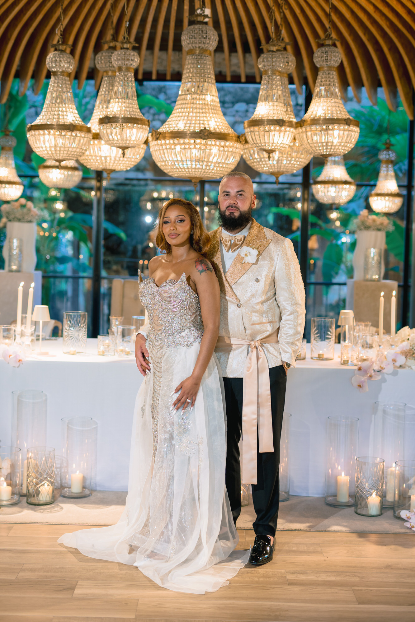 The couple at the sweetheart table before a wall of chandeliers and candles