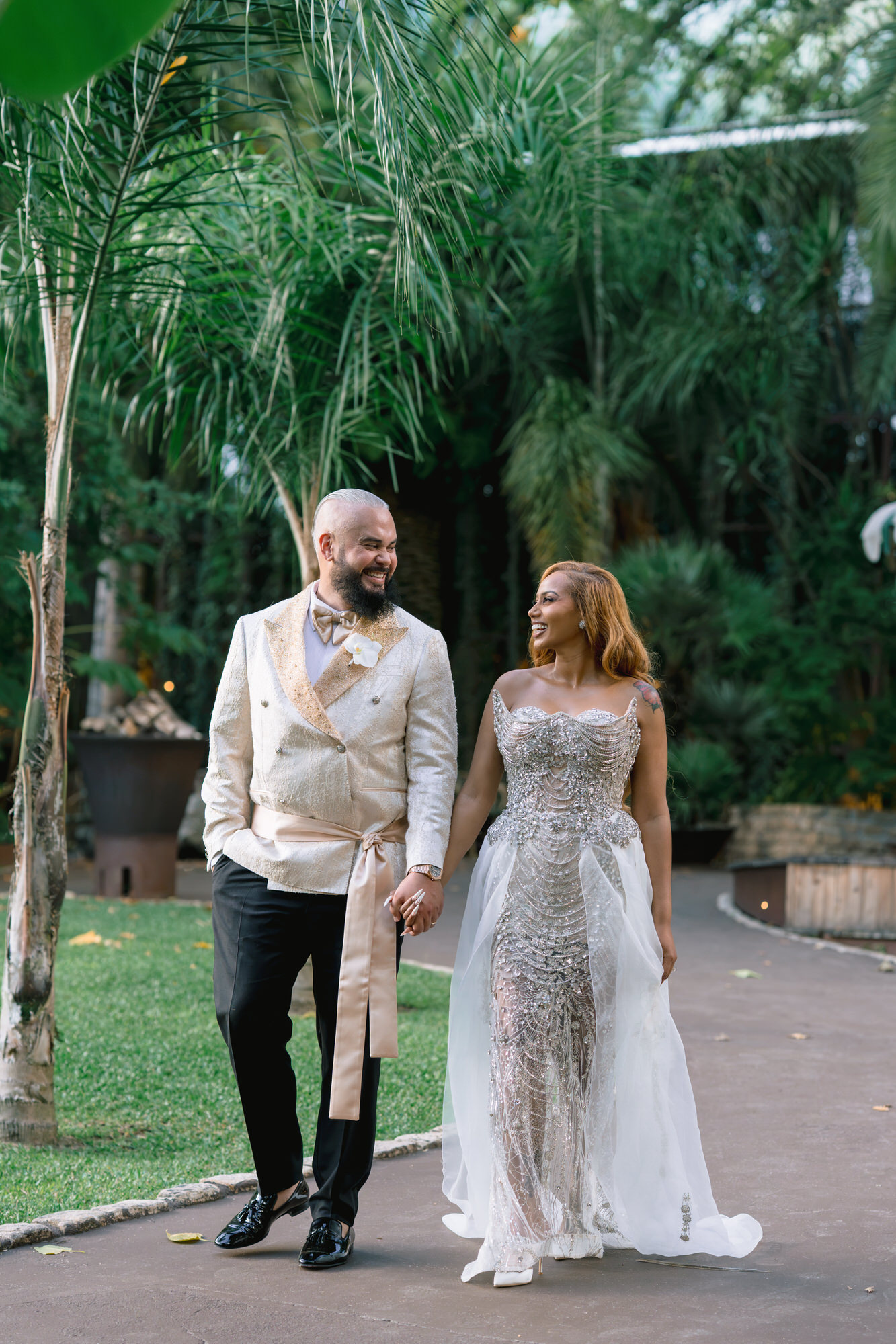 Mahlet and Thomas walking hand in hand beneath palm trees in the garden