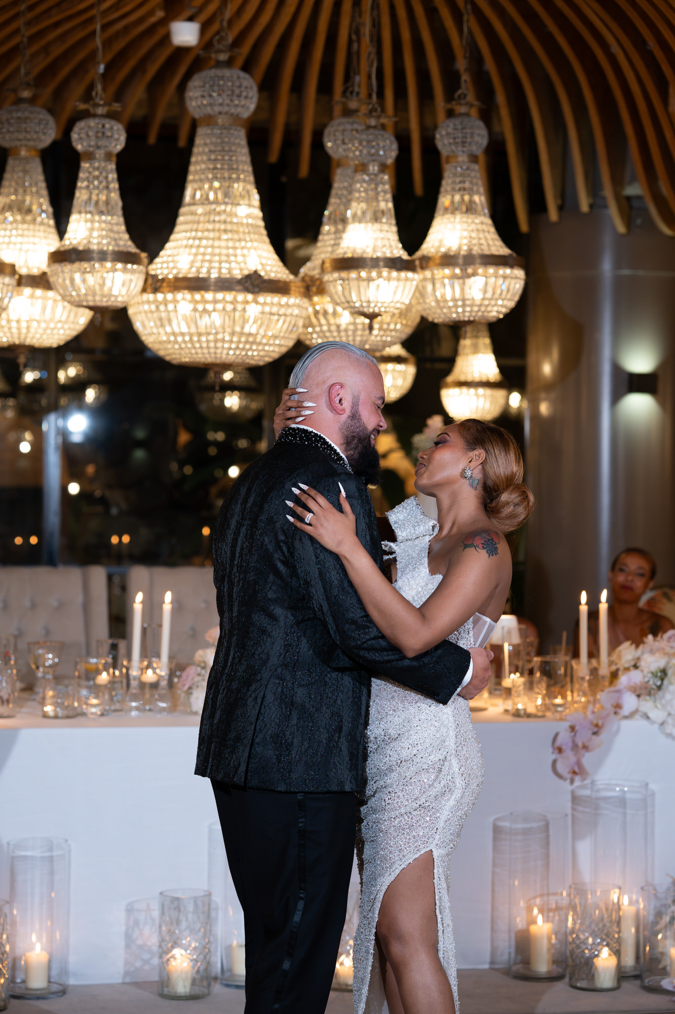 The couple embracing beneath crystal chandeliers in the reception space