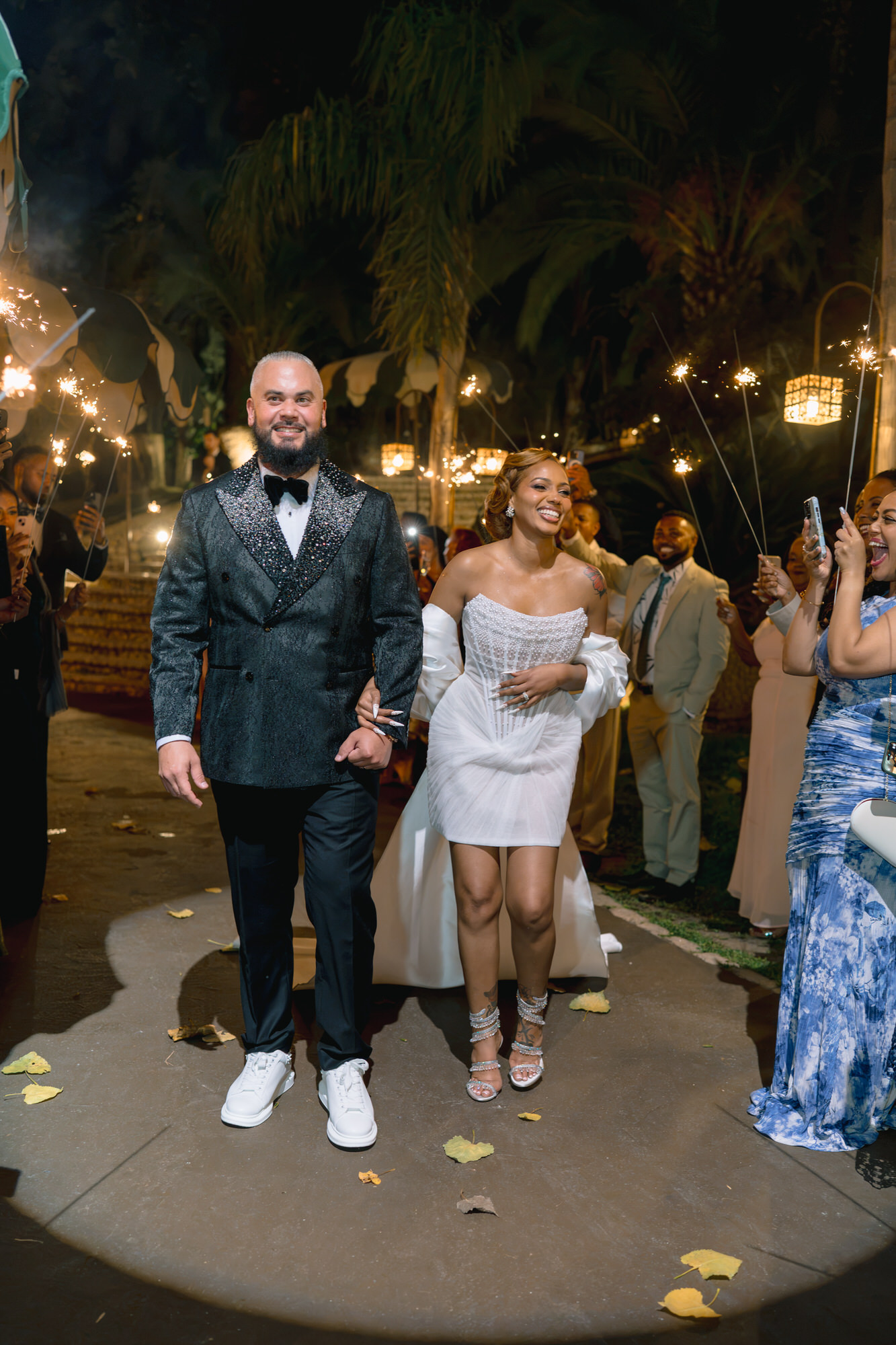 The couple at night among fairy lights, he in a green tuxedo and she in a short white dress