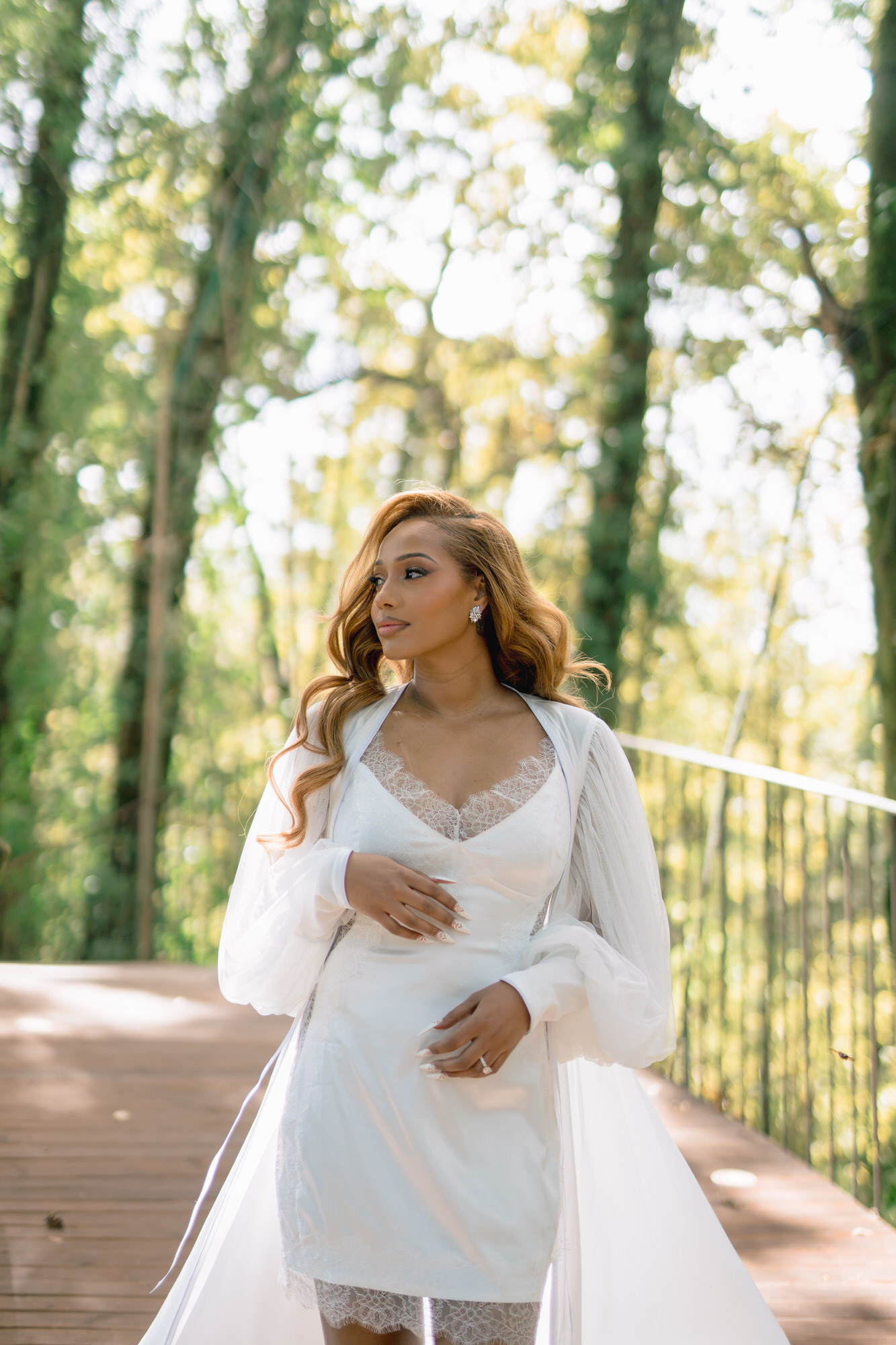 The bride in a white satin robe on a wooden boardwalk among the trees, getting ready
