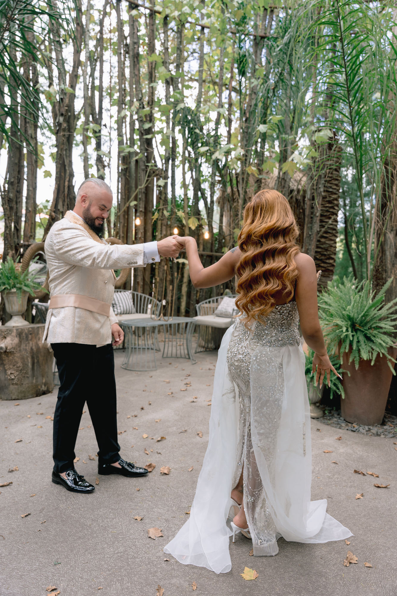 The couple facing each other on a stone path in the woods, hands joined